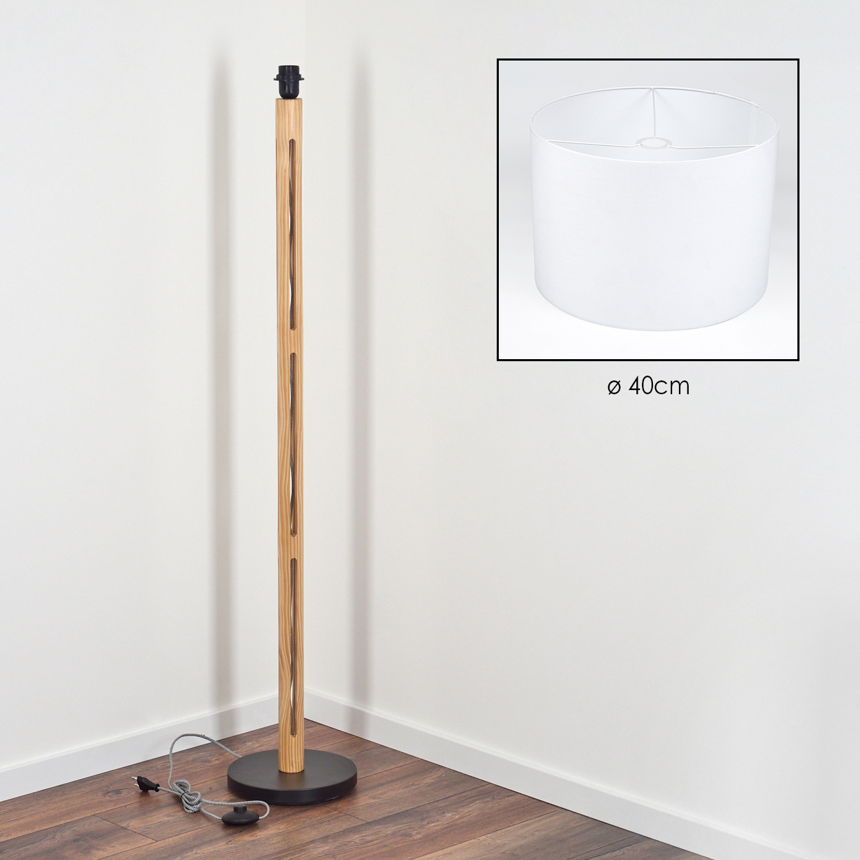 Eine Stehlampe aus Holz mit weißem Lampenschirm. Die Lampe hat einen schwarzen Fuß und einen hellen Holzschaft. Der Lampenschirm ist zylindrisch.