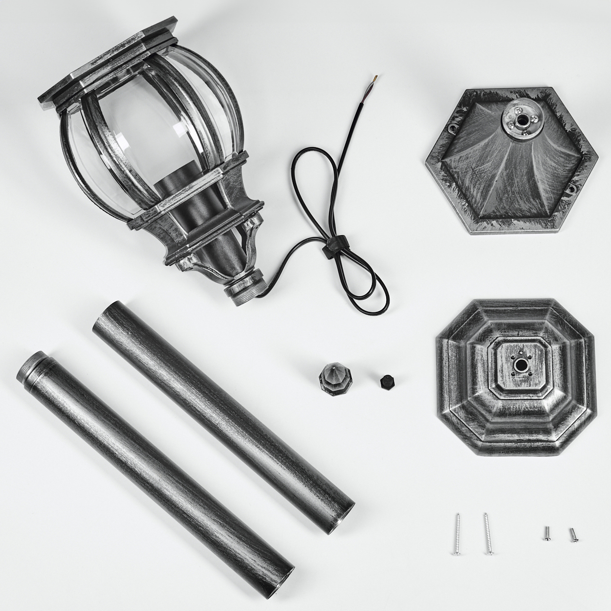 Zerlegte Teile einer Außenlampe: Lampenkopf, Stangen, Sockel, Schrauben und Verkabelung, alles auf weißem Untergrund, Draufsicht.