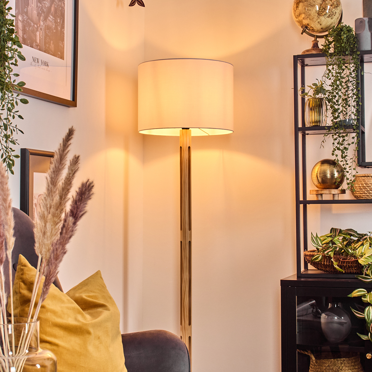 Raumecke mit Stehlampe, Pflanzen, Globus und gerahmter Kunst. Im Vordergrund ein Sofa mit Kissen.
