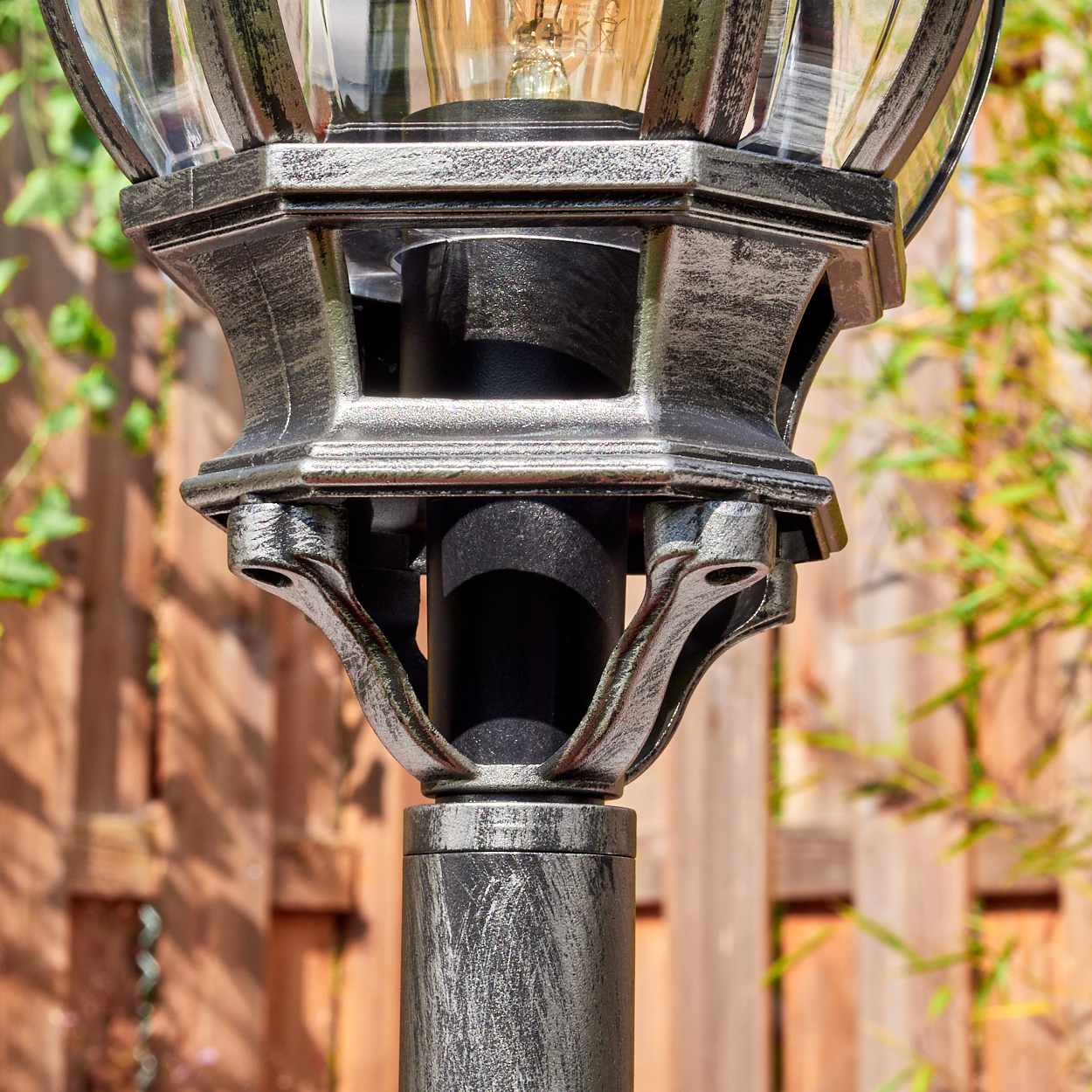 Nahaufnahme einer dekorativen Laterne. Die Lampe hat eine silberne und schwarze Oberfläche mit Glaskugel. Im Hintergrund ein Holzzaun.