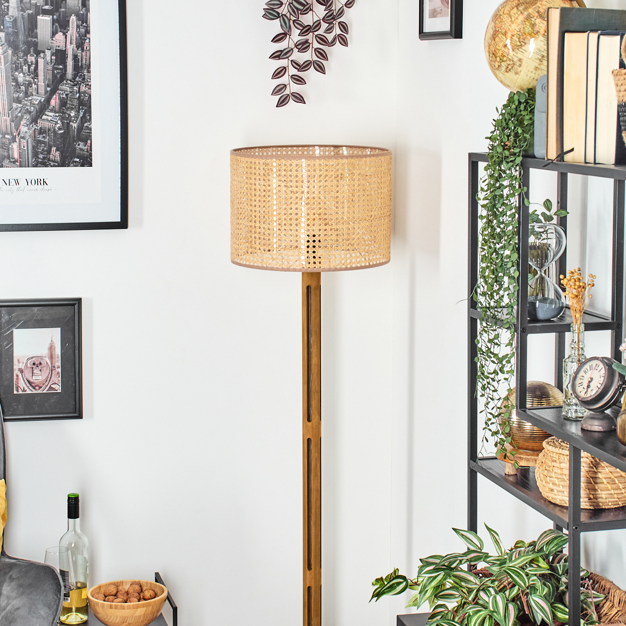 Ein Raum mit einer Lampe, einem Regal mit Dekorationen und gerahmten Bildern. Die Lampe ist hoch mit einem gewebten Schirm. Pflanzen und ein Globus stehen auf dem Regal.