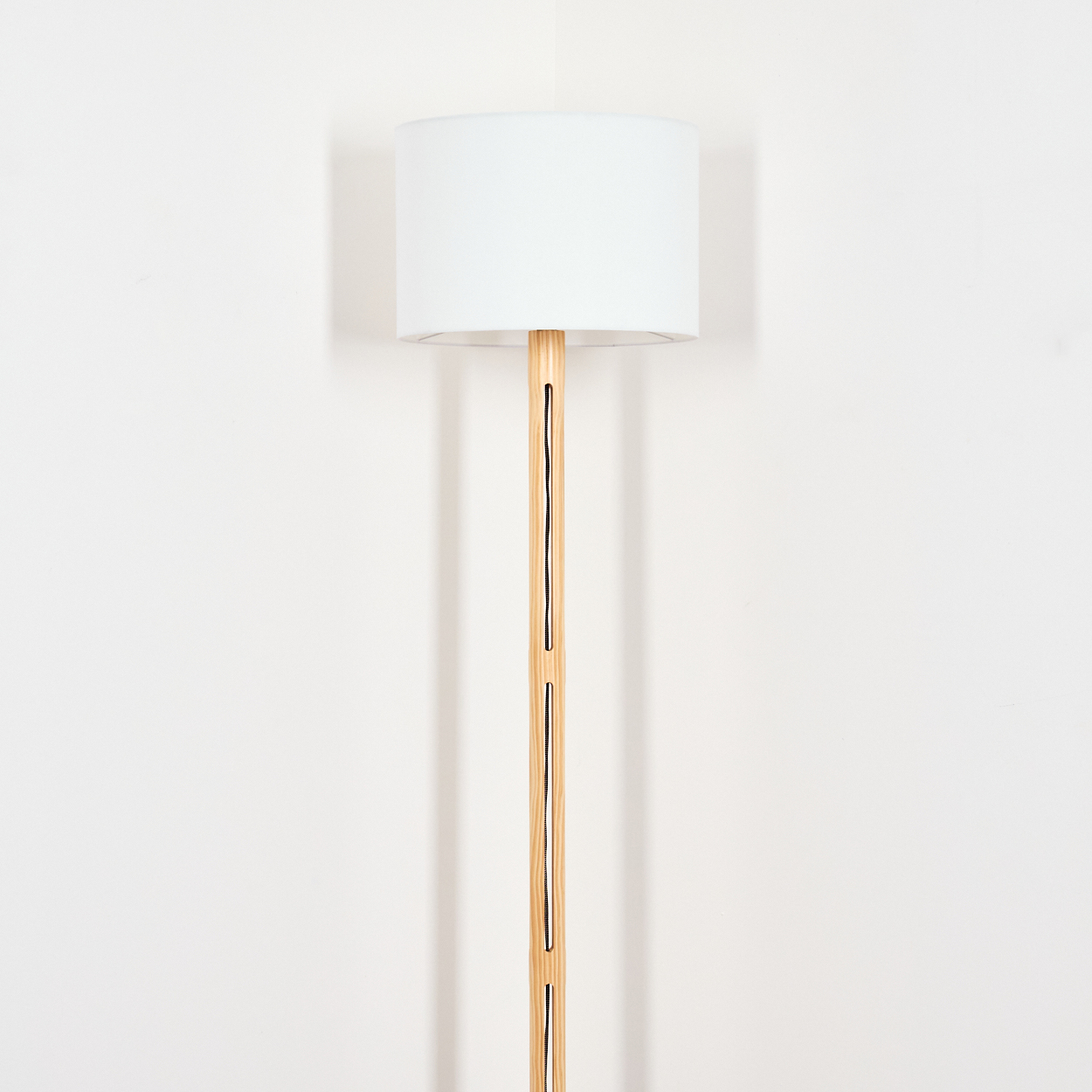 Eine moderne Stehlampe mit weißem Lampenschirm und Holzstiel. Der Hintergrund ist eine schlichte weiße Wand.