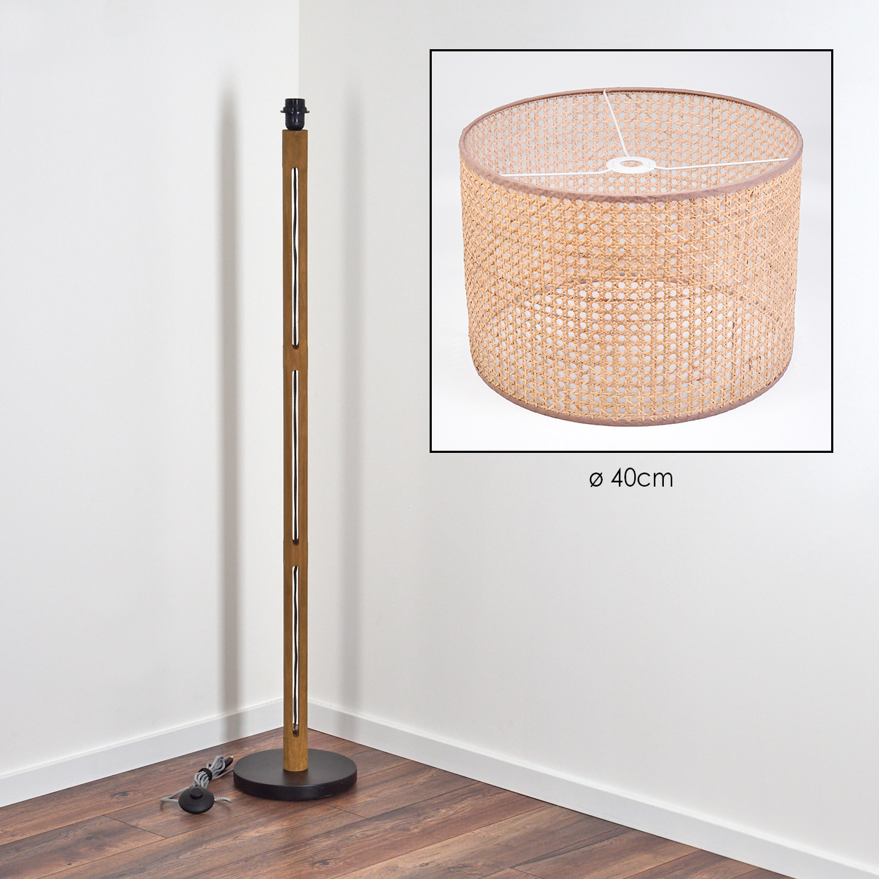 Eine Stehlampe aus Holz mit einem gewebten Lampenschirm. Der Lampenschirm ist kreisförmig, hellbraun. Die Lampe steht in einer weiss getünchten Ecke.