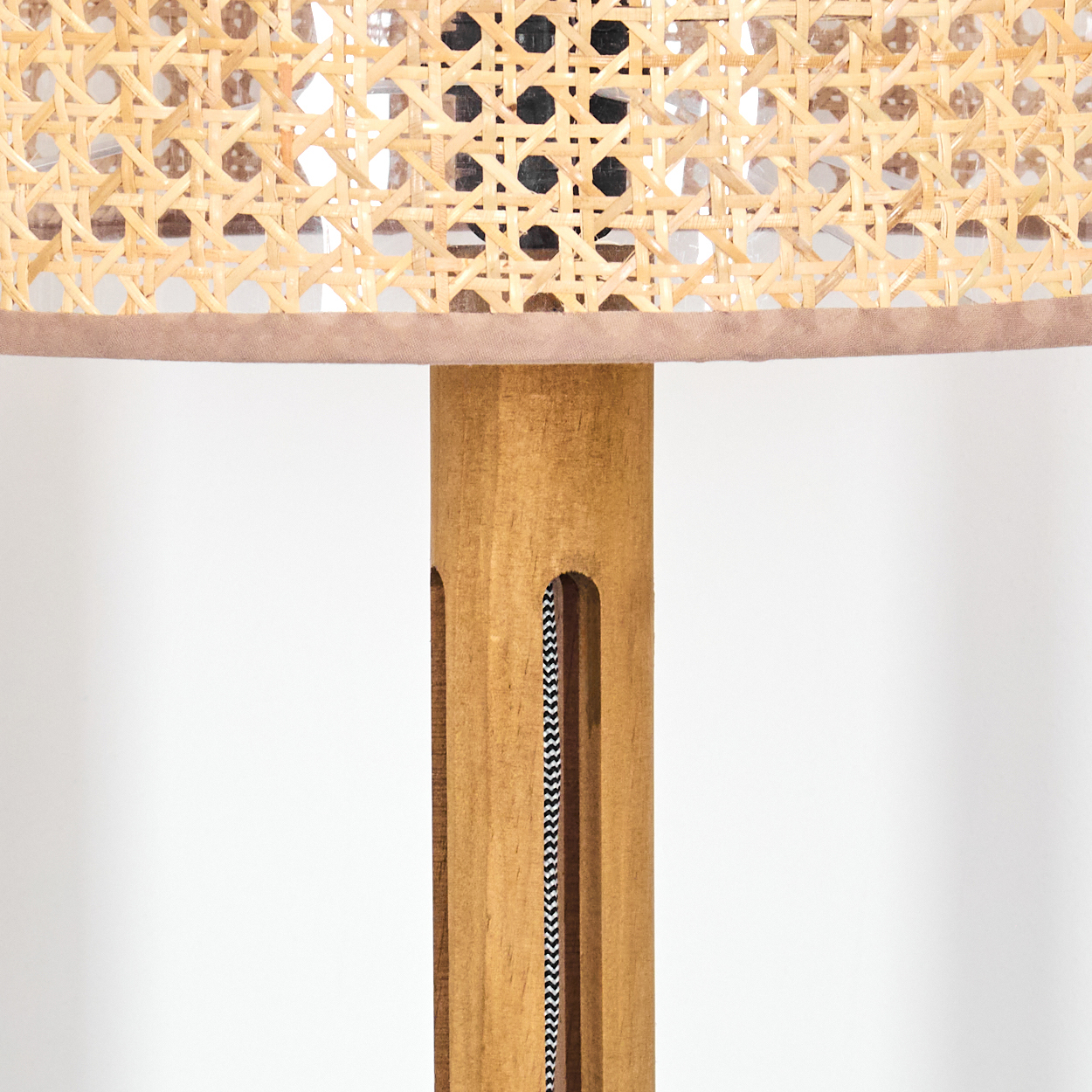 Nahaufnahme einer Lampe. Gewebter Schirm, Holzpfosten mit Ausschnitten und ein schwarz-weißes Zickzack-Kabel. Beige- und hellbraune Farben.