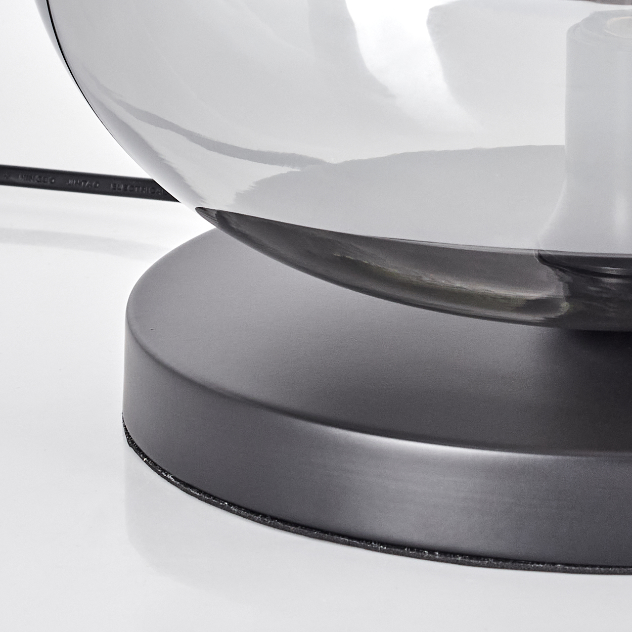 Nahaufnahme einer Lampe. Ein grauer Glasschirm sitzt auf einem dunkelgrauen Sockel. Ein schwarzes Kabel ist sichtbar.