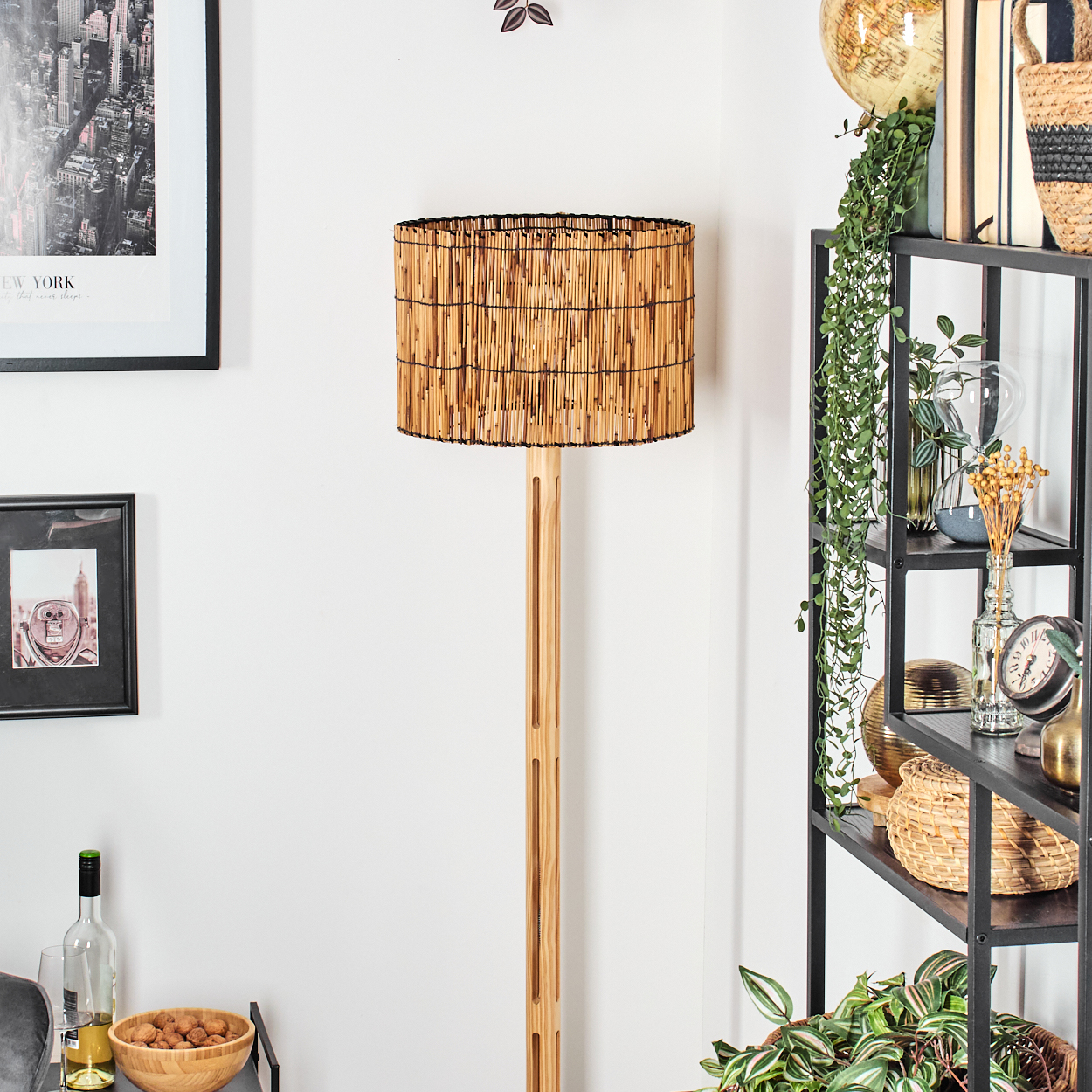 Eine Stehlampe mit Bambusschatten steht in einem Raum mit einem Regal. Kunstwerke und Dekorationsartikel sind sichtbar.