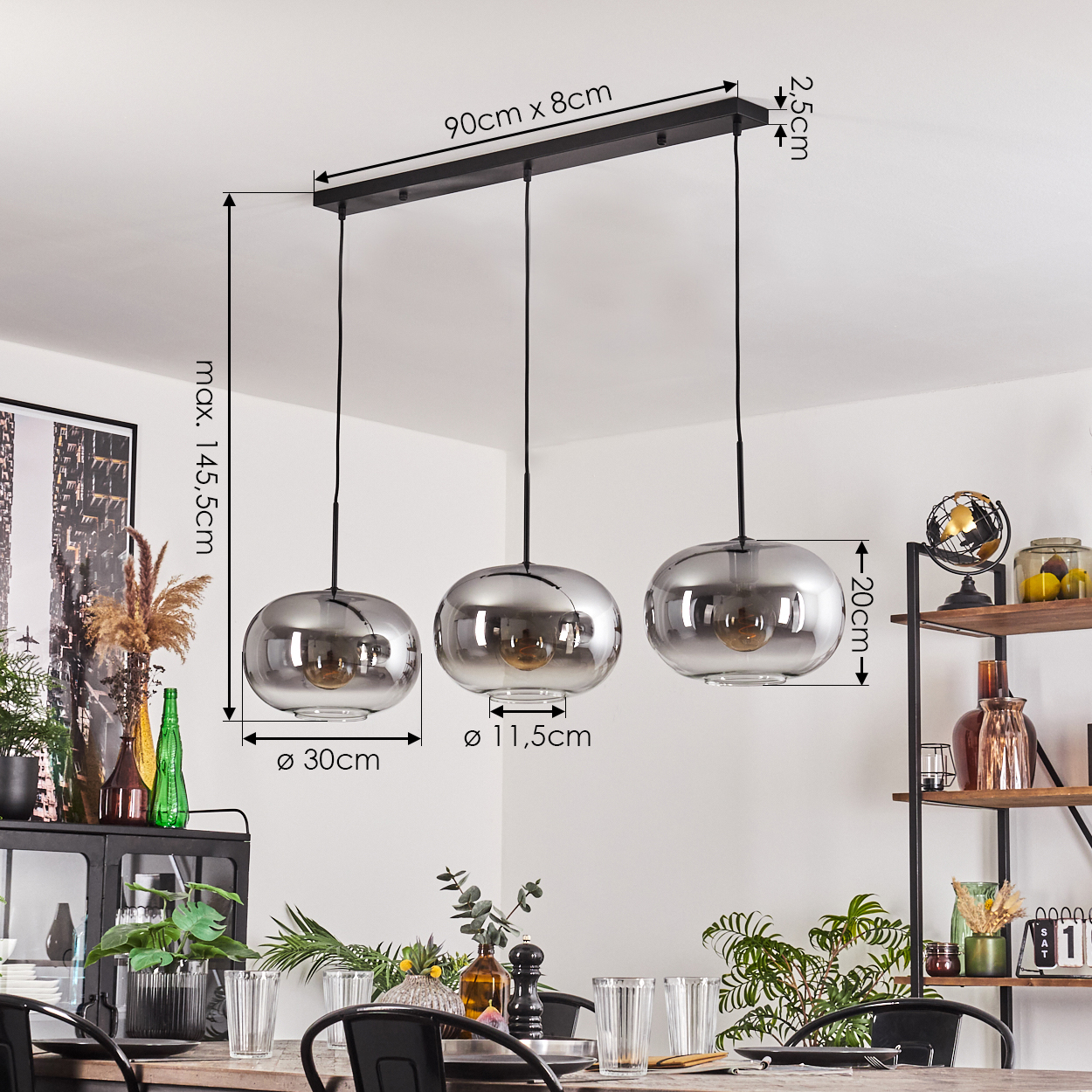 Drei silberne Pendelleuchten über einem Esstisch mit Pflanzen, Gläsern und einem schwarzen Metallschrank mit Regalen.