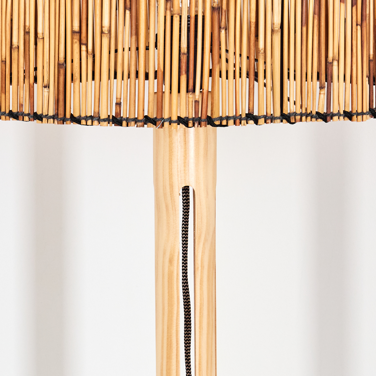 Nahaufnahme einer Lampe aus Bambus und Holz. Der Lampenschirm besteht aus Bambusstäben, der Sockel aus Holz mit einer schwarzen Schnur.