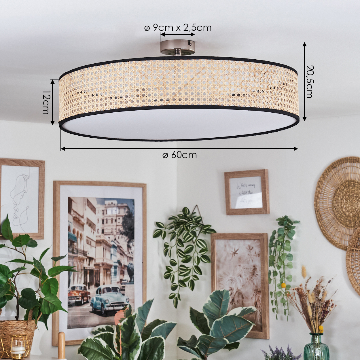 Eine Deckenlampe aus geflochtenem Rattan mit schwarzer Zierleiste ist an einer weißen Decke befestigt. Kunstwerke und Pflanzen schmücken die weiße Wand.
