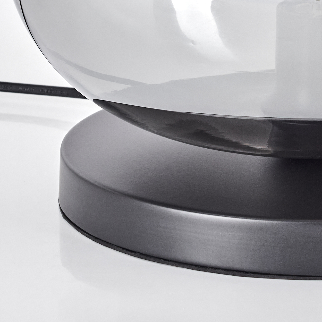 Nahaufnahme einer Lampe. Der Sockel ist grau und kreisförmig und trägt einen klaren, kugelförmigen Schirm mit einem sichtbaren Kabel.