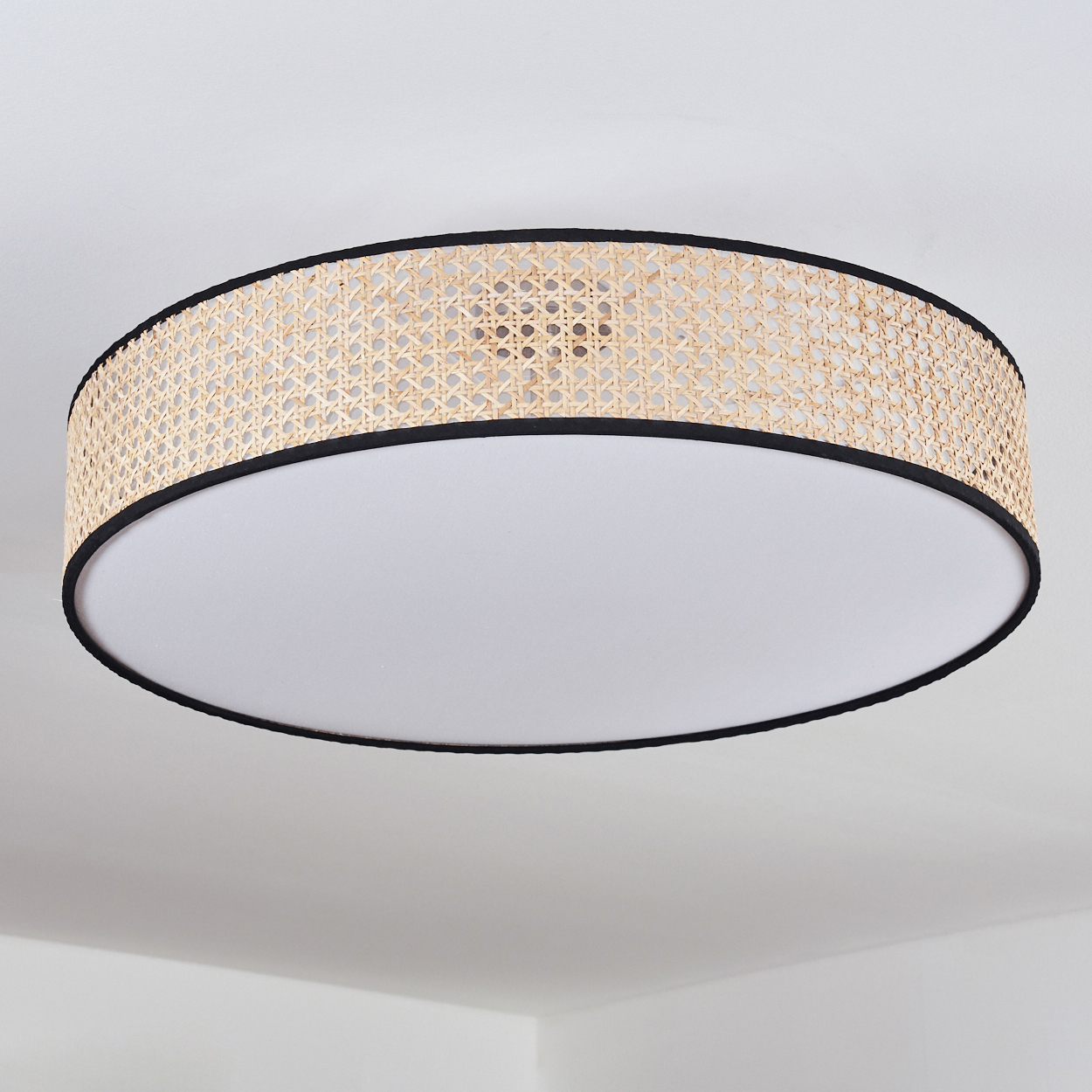 Eine runde Deckenlampe mit gewebtem Rattanschatten und schwarzem Rand, über einem weißen Diffusor, an einer weißen Decke montiert.