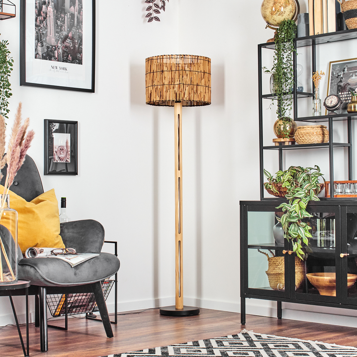 Ein Raum mit einer Stehlampe. Es gibt einen grauen Stuhl mit einem gelben Kissen. Ein schwarzes Regal mit Pflanzen und Dekoration ist im Hintergrund.
