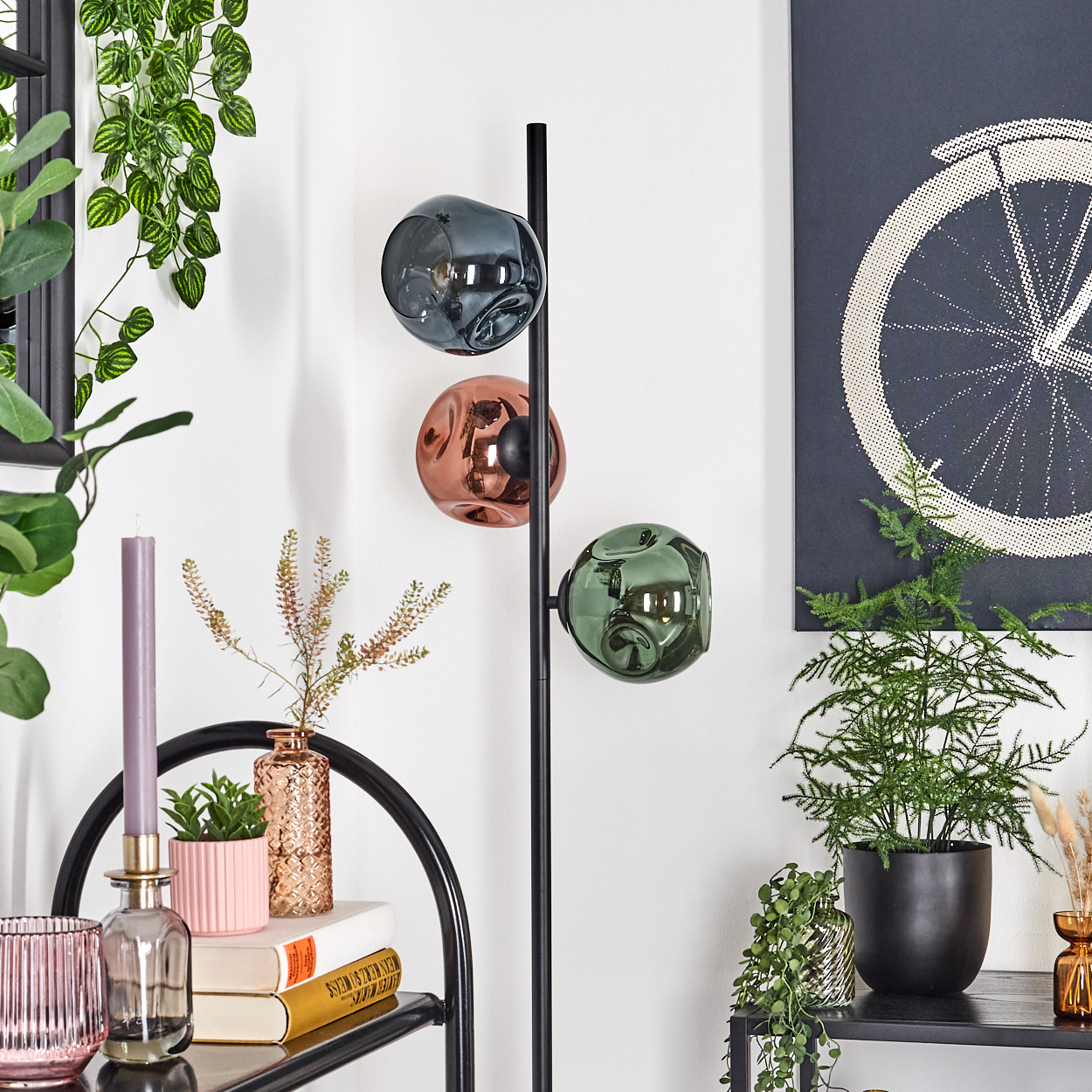 Ein modernes Wohnzimmer mit einer schwarzen Lampe mit drei Kugelleuchten. Pflanzen und dekorative Gegenstände sind angeordnet.