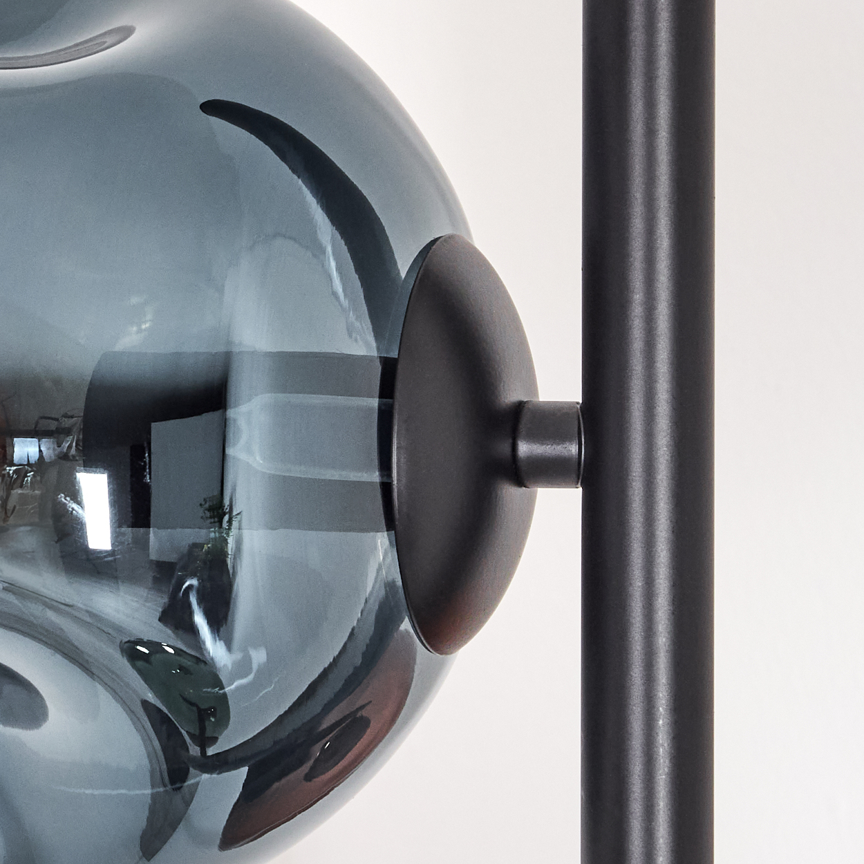 Nahaufnahme einer modernen Lampe. Eine graue Glaskugel ist mit einer schwarzen Metallsäule und einer schwarzen runden Scheibe verbunden. Weißer Hintergrund.