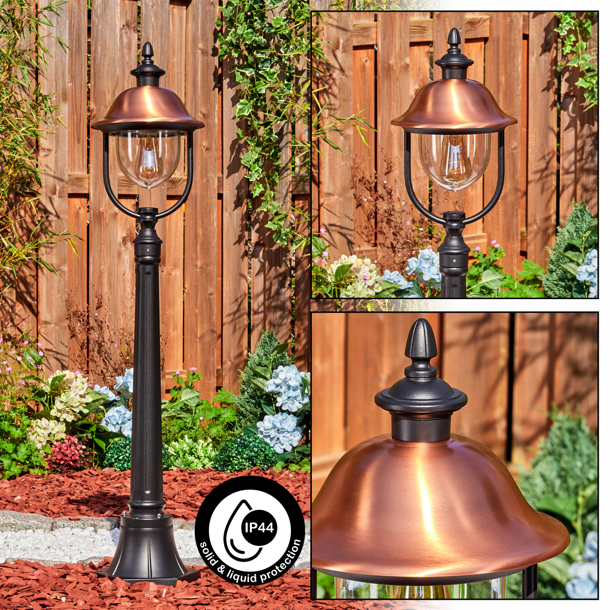 Eine bronzefarbene Außenlampe steht in einem Garten. Die Lampe hat einen schwarzen Pfosten und einen kupferfarbenen Kopf. Im Hintergrund ist ein Holzzaun.