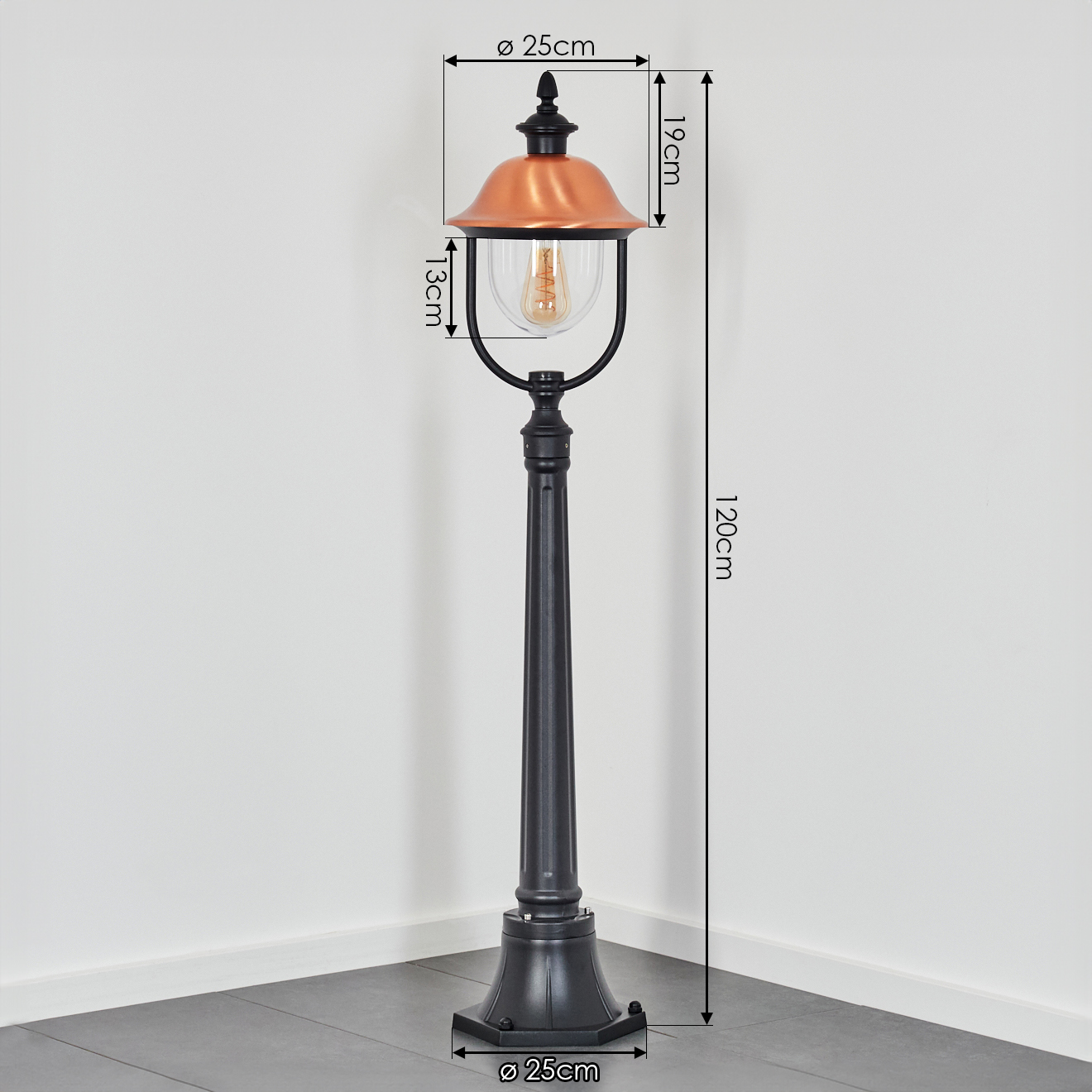 Schwarze Außenlampe mit kupferfarbener Oberseite und klarem Glas. Sie hat ein Vintage-Design. Der Hintergrund ist eine weiße Wand.