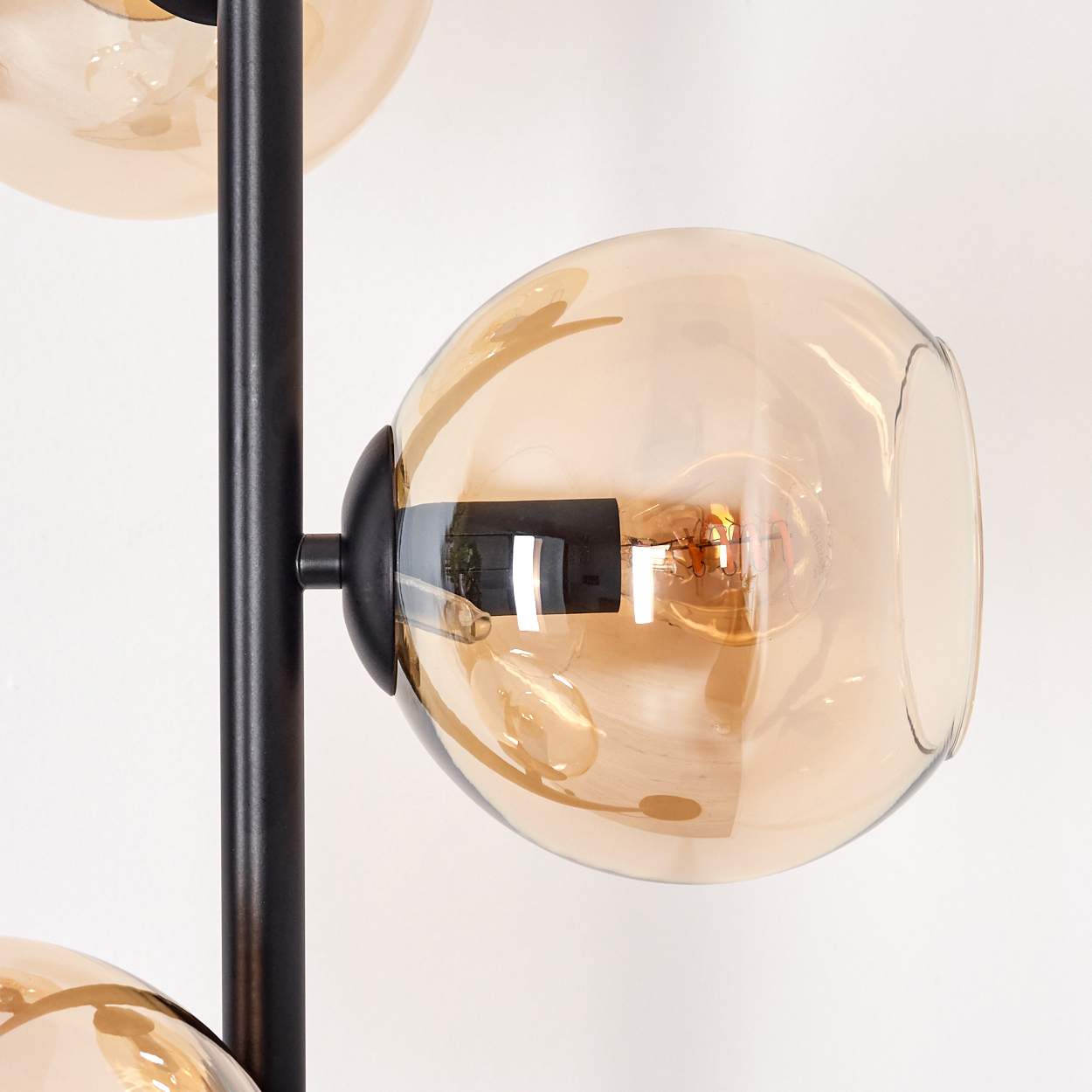 Eine moderne Lampe mit drei Glaskugeln. Jede Kugel hat eine Glühbirne. Der Rahmen der Lampe ist schwarz, vor einer weißen Wand.