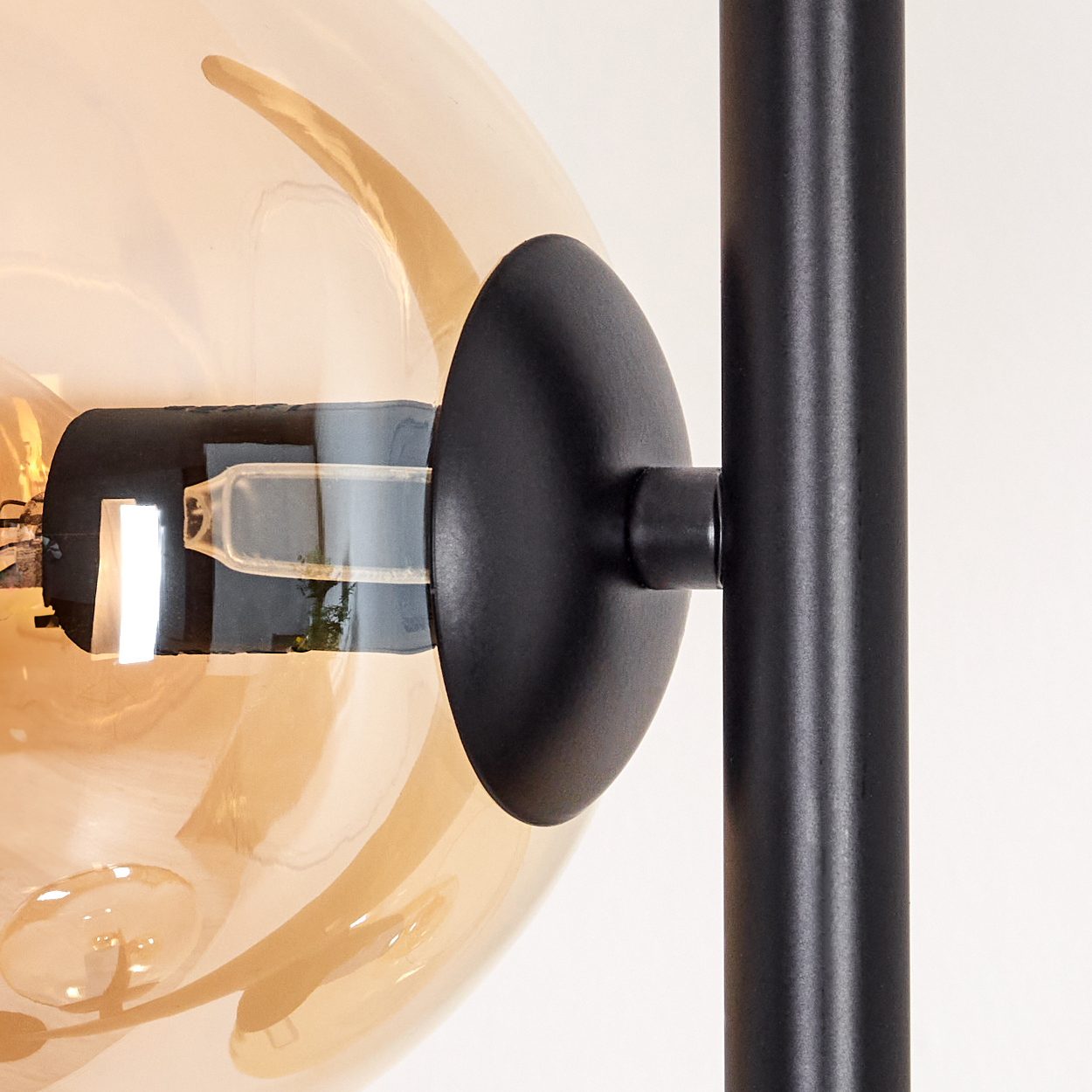 Nahaufnahme einer modernen Lampe. Sie hat einen runden, bernsteinfarbenen Glasschirm, eine schwarze Halterung und eine schwarze Stange.