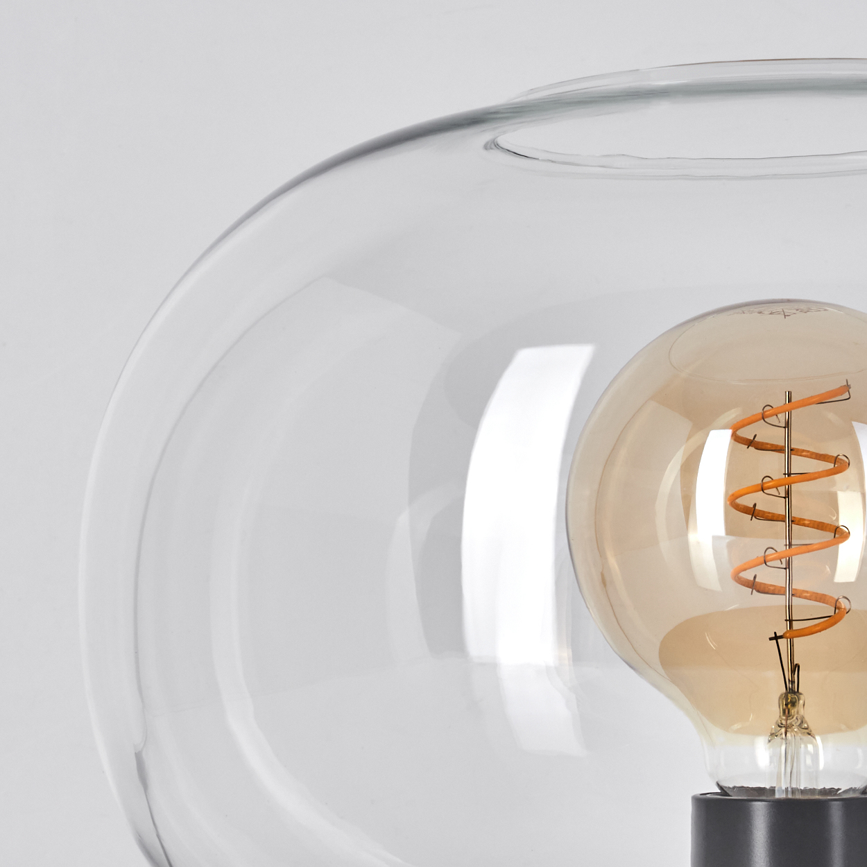 Eine klare Glaslampe mit einer Wendelglühbirne. Die Lampe befindet sich in einer klaren Glaskugel.