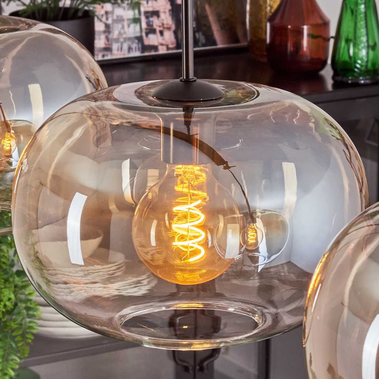 Nahaufnahme von Glas-Pendelleuchten. Jede hat einen kugelförmigen Schirm mit einer sichtbaren, beleuchteten Glühbirne im Inneren.