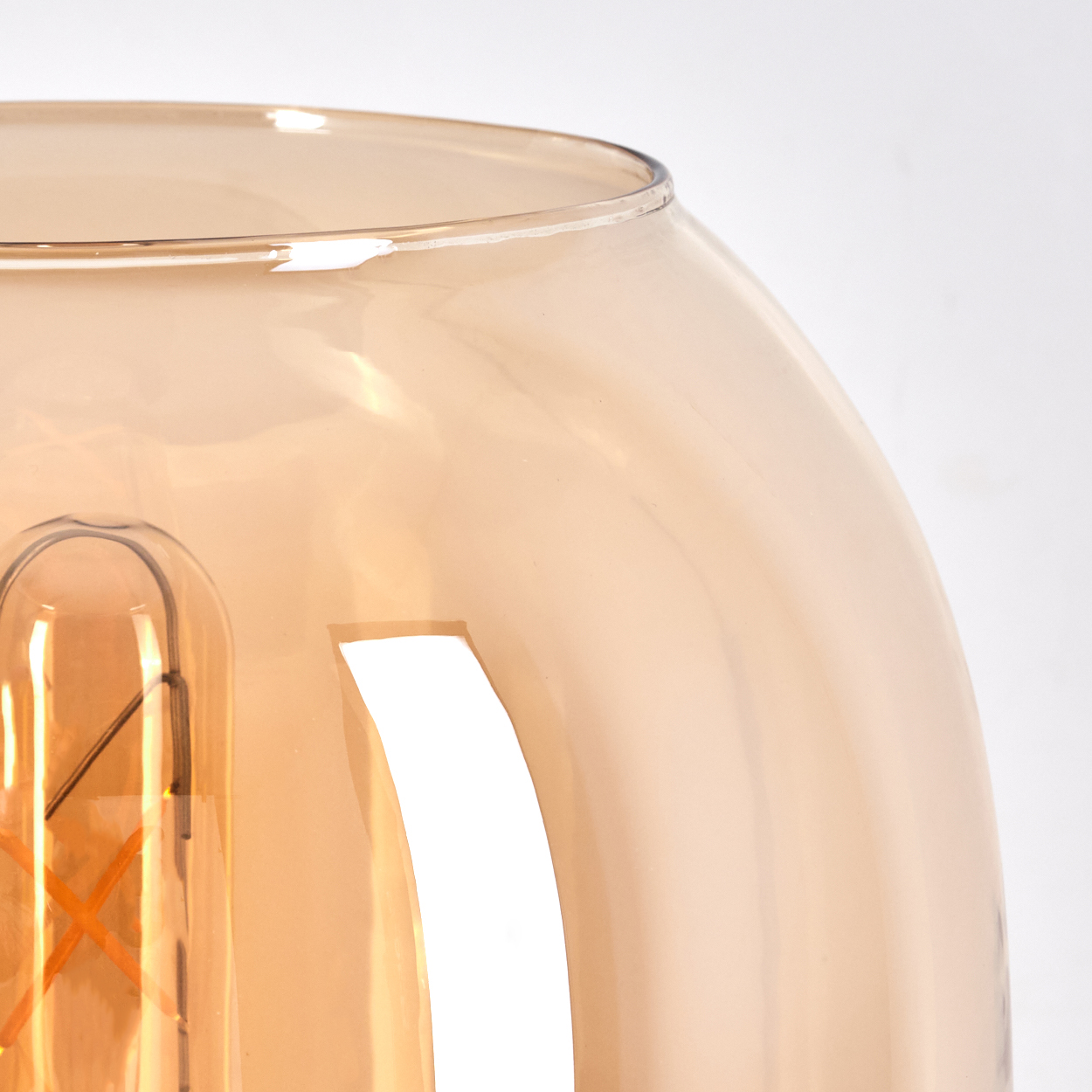 Nahaufnahme einer Glaslampe mit Glühbirne. Das Glas ist bernsteinfarben, der Hintergrund weiß.