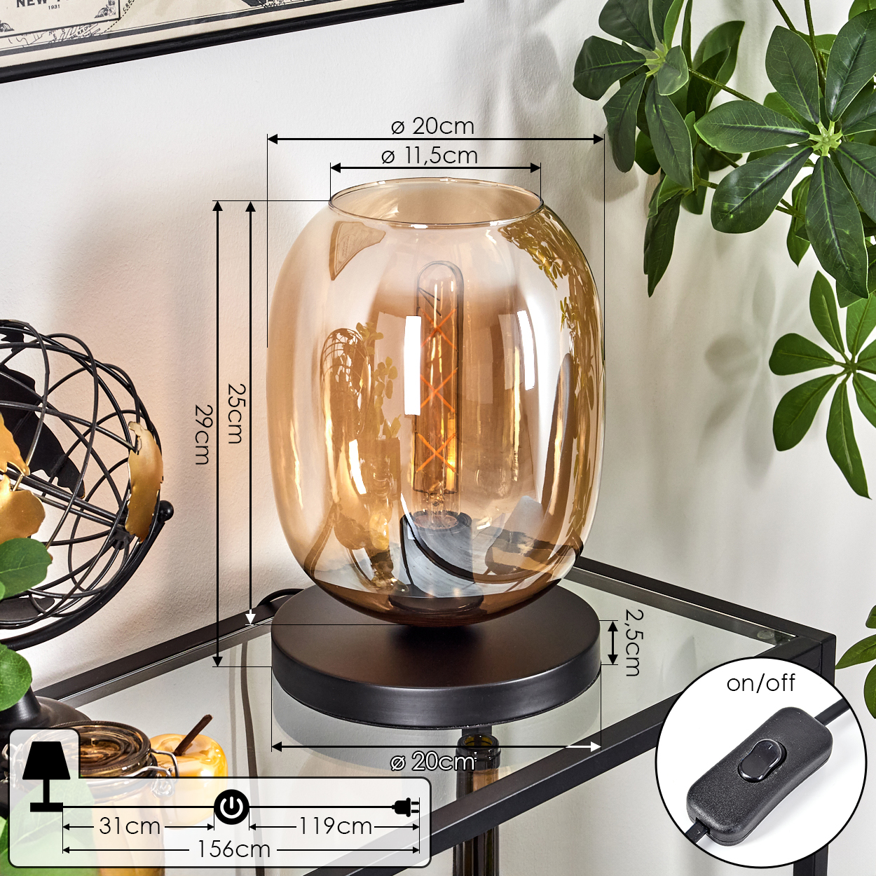 Eine dekorative Lampe mit braunem Glasschirm. Sie steht auf einem schwarzen Sockel auf einem Glastisch. Rechts ist eine grüne Pflanze.