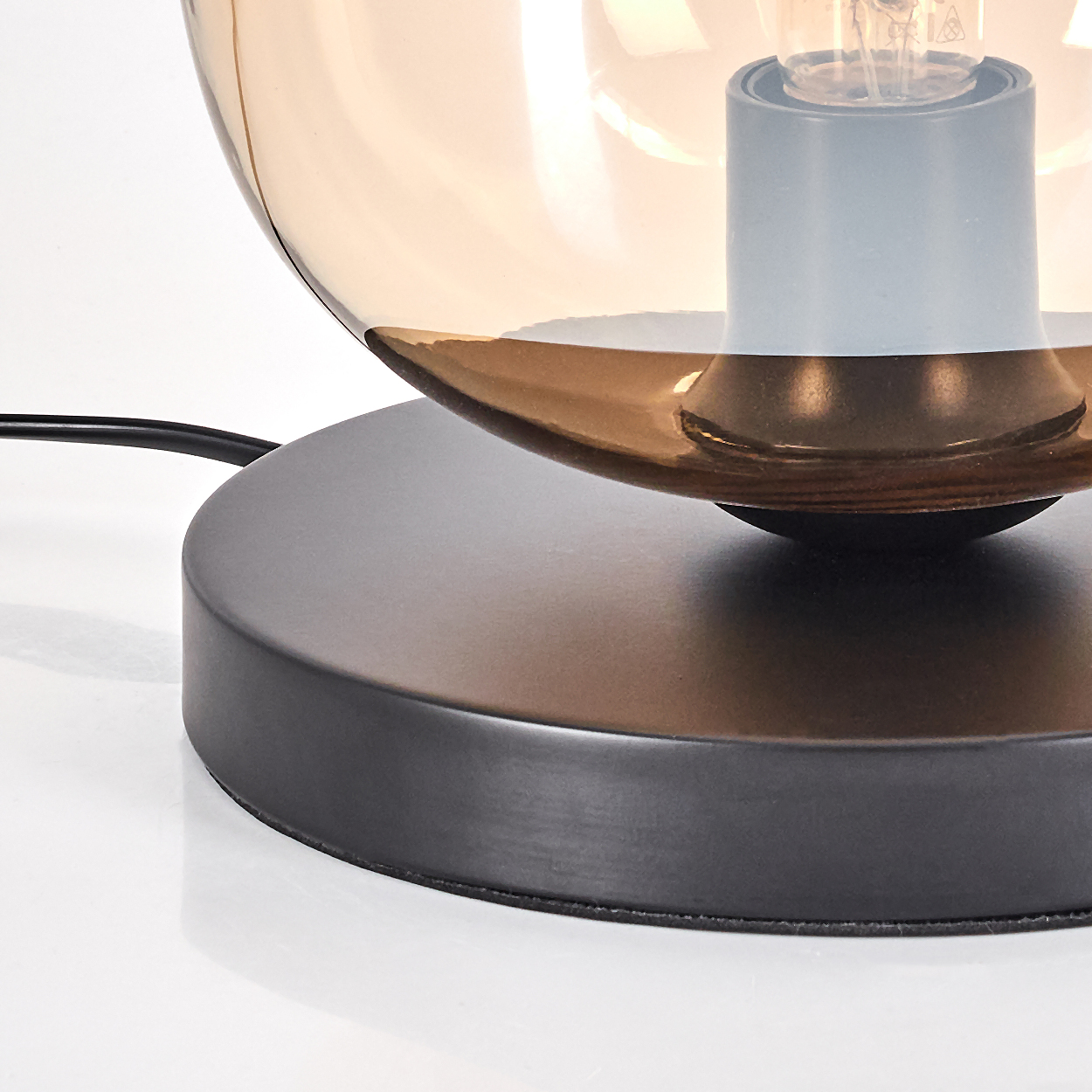 Nahaufnahme einer Tischlampe. Sie hat einen bronzefarbenen Glasschirm, eine Glühbirne und einen schwarzen Sockel.