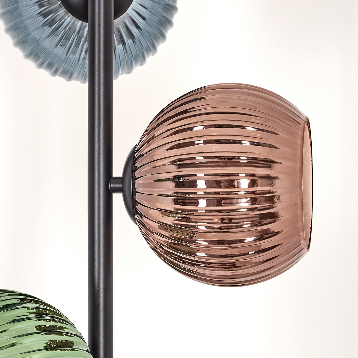 Eine moderne Lampe mit drei Glasschirmen in Blau, Kupfer und Grün. Die Schirme sind gerippt und kugelförmig, vor weißem Hintergrund.