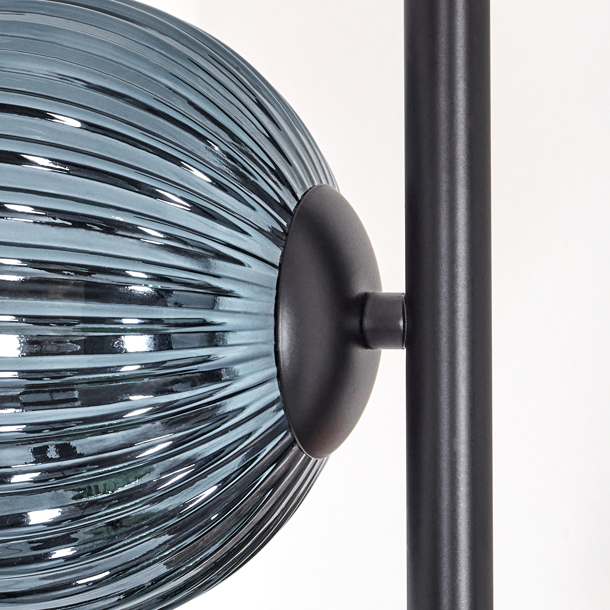Nahaufnahme einer Lampe mit teal, geriffelter Glasschirm und schwarzem Metallträger. Der Hintergrund ist weiß.
