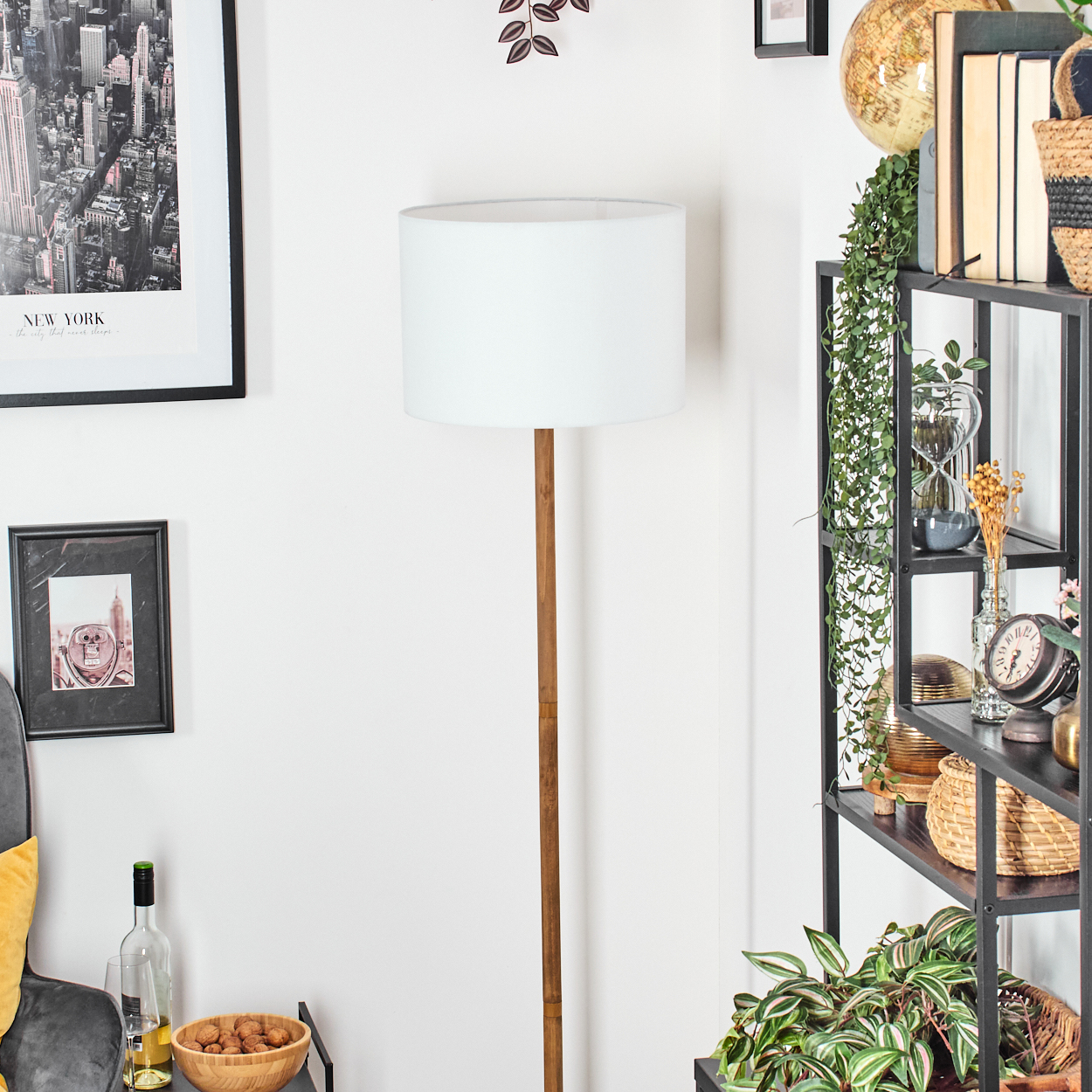 Ein Raum mit einer weißen Lampe, einem Holzständer und einem schwarzen Bücherregal mit verschiedenen Gegenständen und Pflanzen.