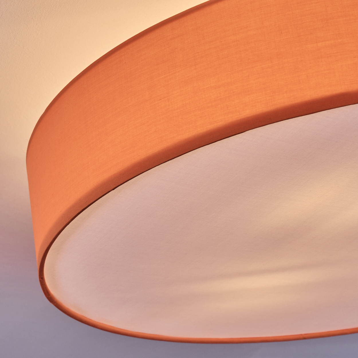 Nahaufnahme eines Lampenschirms. Der Lampenschirm ist außen orange und innen weiß. Der Hintergrund ist ein Gradient aus Weiß und Grau.
