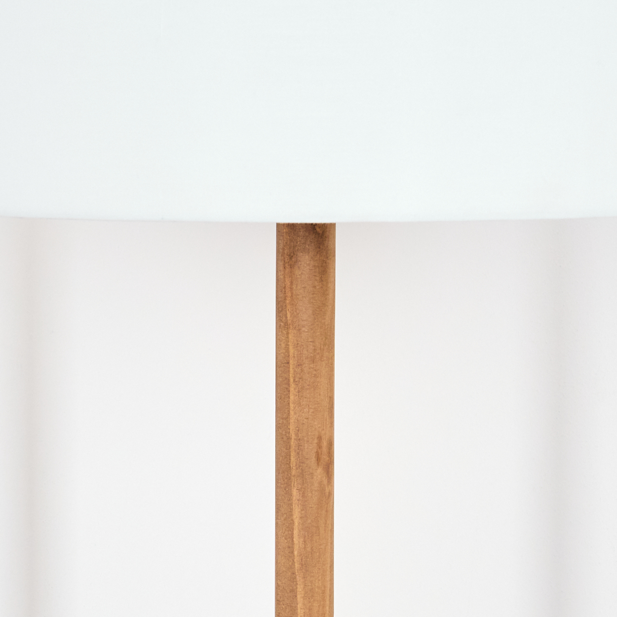Nahaufnahme einer Lampe. Ein weißer Lampenschirm sitzt über einer braunen Holzstange auf weißem Hintergrund.