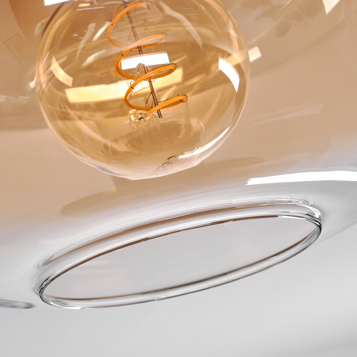 Nahaufnahme einer Glühbirne mit goldener Wendel, eingebettet in eine klare Glasvorrichtung mit reflektierender Oberfläche.