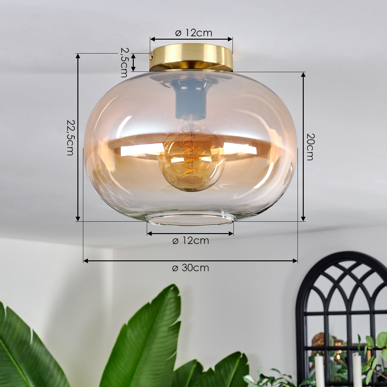 Eine moderne Deckenleuchte mit Glasschirm und goldenem Sockel. Maße sind beschriftet. Pflanzen und ein Fensterrahmen im Hintergrund.