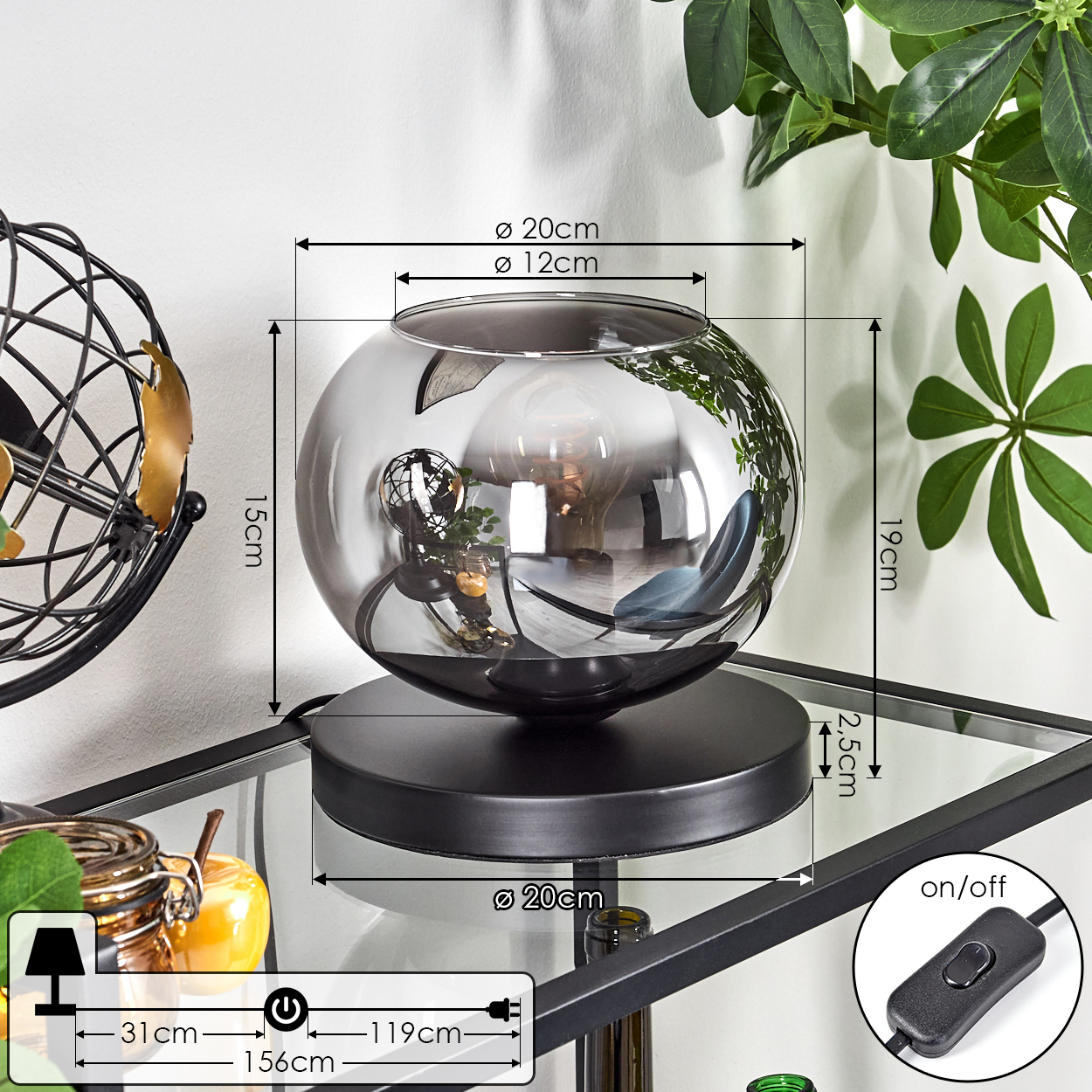Eine dekorative Lampe mit rauchfarbenem Glasschirm steht auf einem Glasregal. Ein Ein-/Ausschalter und Maße sind ebenfalls zu sehen.