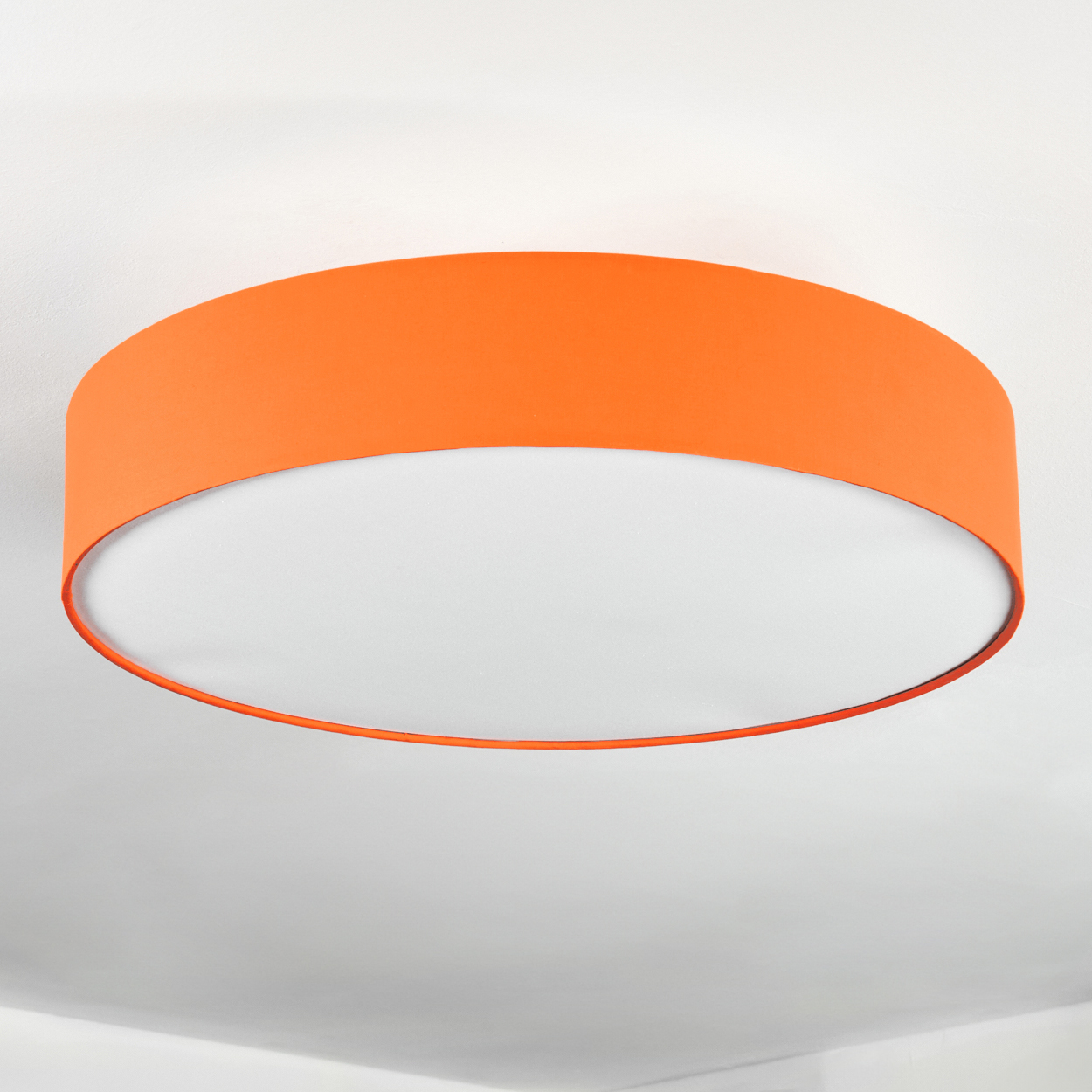 Ein orangefarbener Lampenschirm ist an einer weißen Decke befestigt. Der Lampenschirm hat eine zylindrische Form und ein weißes, kreisförmiges Licht.