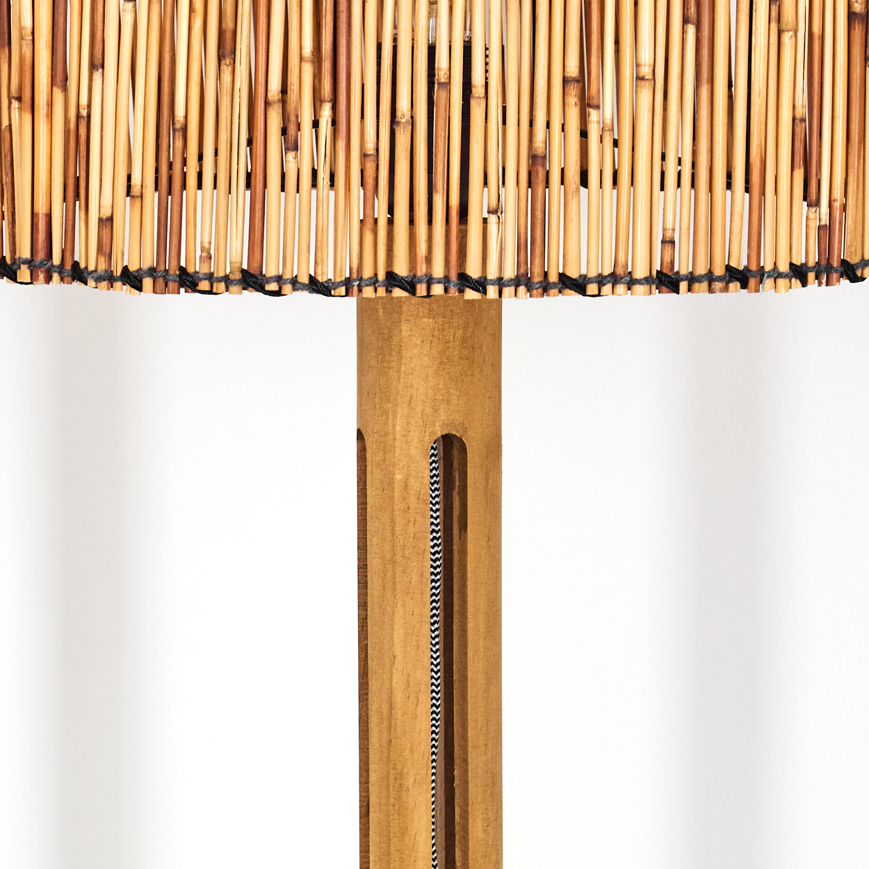 Eine Lampe mit Bambusschirm und Holzständer. Der Ständer hat ein schwarz-weißes Zickzack-Muster-Kabel.
