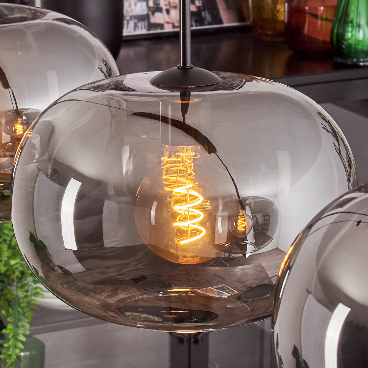 Nahaufnahme von Pendelleuchten mit Glaskugeln. Innen leuchten gewendelte Glühbirnen. Die Kugeln sind grau und reflektieren Licht.