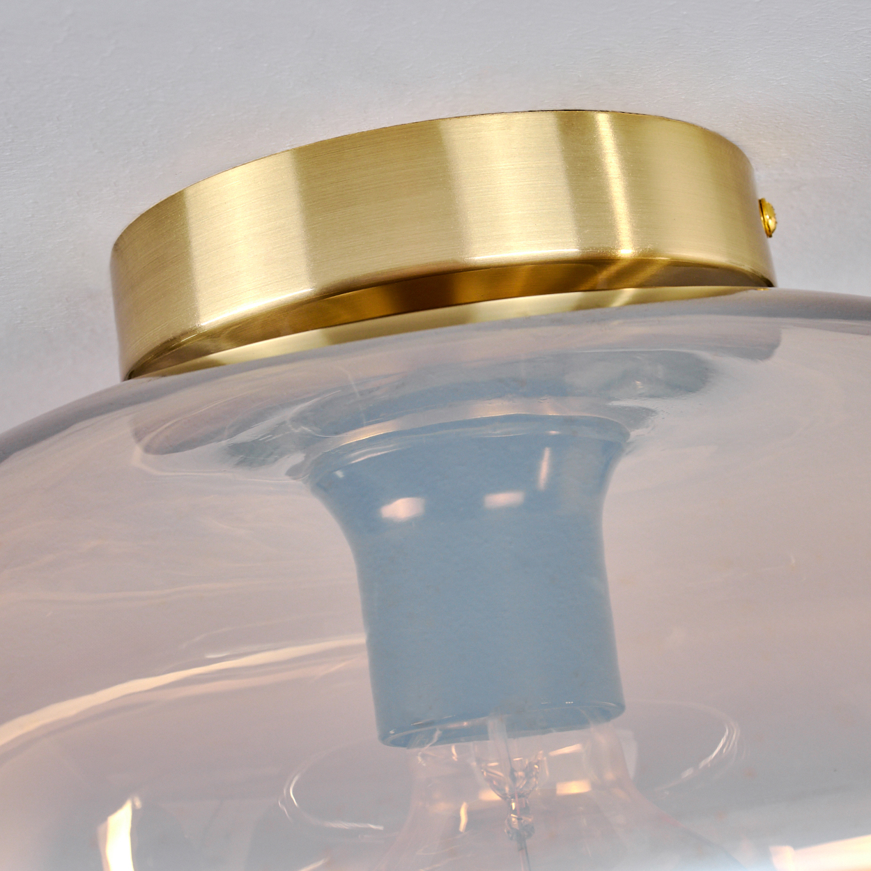 Nahaufnahme einer modernen Leuchte. Sie hat einen goldfarbenen Metallsockel und einen Glasschirm mit blau-grauem Stiel, Glühbirne sichtbar.