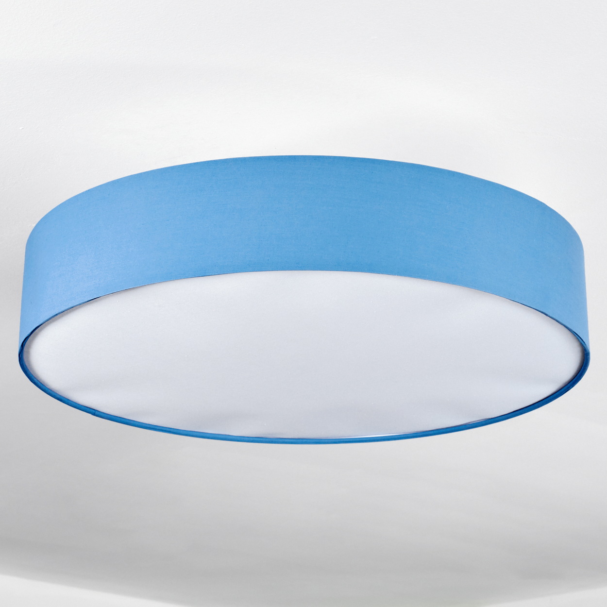 Ein runder, blauer Lampenschirm mit weißem Innenraum hängt an einer weißen Decke. Die Lampe hat eine zylindrische Form.