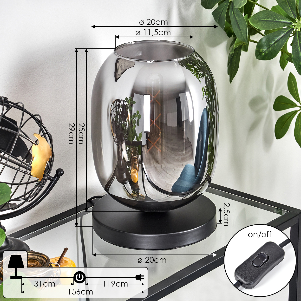 Eine dekorative Lampe mit Abmessungen steht auf einem Glastisch. Sie hat einen Rauchglasschirm und einen schwarzen Sockel. Ein Schalter und Blätter sind vorhanden.