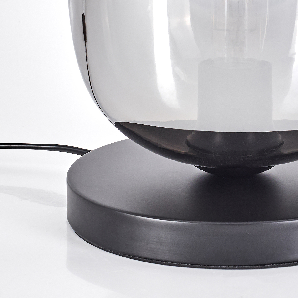 Nahaufnahme einer modernen Lampe. Sie hat einen runden, rauchfarbenen Glasschirm und einen schwarzen Sockel. Das Netzkabel ist sichtbar.