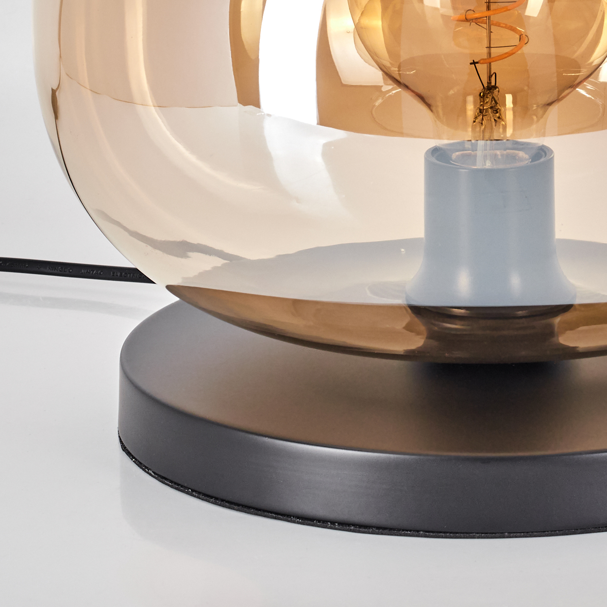 Eine moderne Lampe mit braunem Glasschirm und sichtbarer Glühbirne. Der Sockel ist schwarz und der Hintergrund weiß.