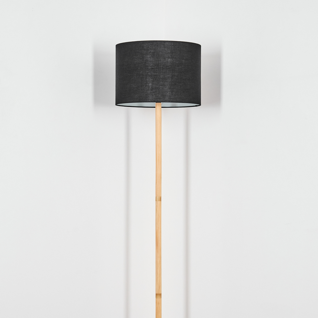 Eine Stehlampe mit schwarzem Lampenschirm und Holzfuß steht vor einer weißen Wand.