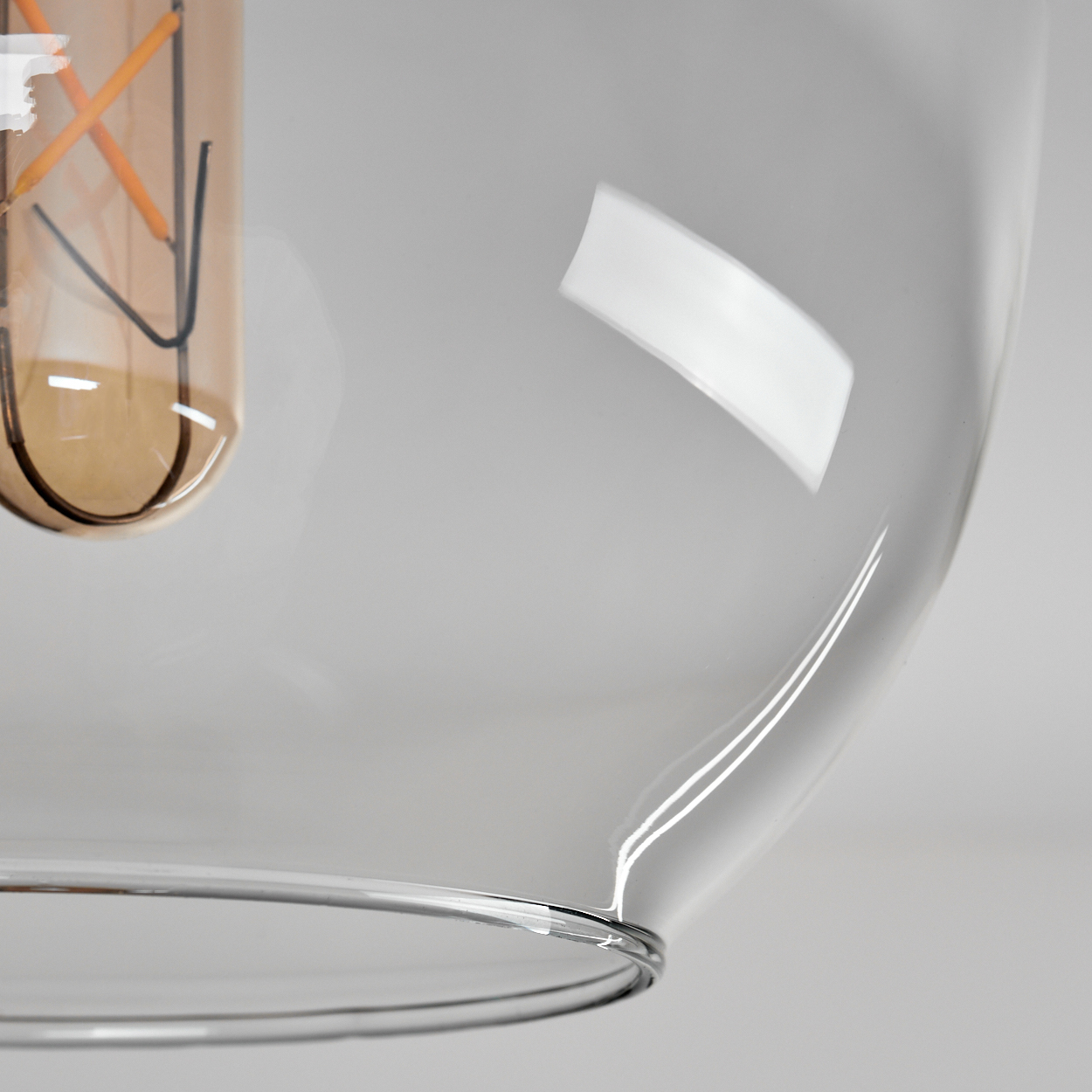 Nahaufnahme einer Glasleuchte. Ein klarer Glasschirm mit einer sichtbaren Edison-Glühbirne. Der Hintergrund ist ein sanftes Grau.