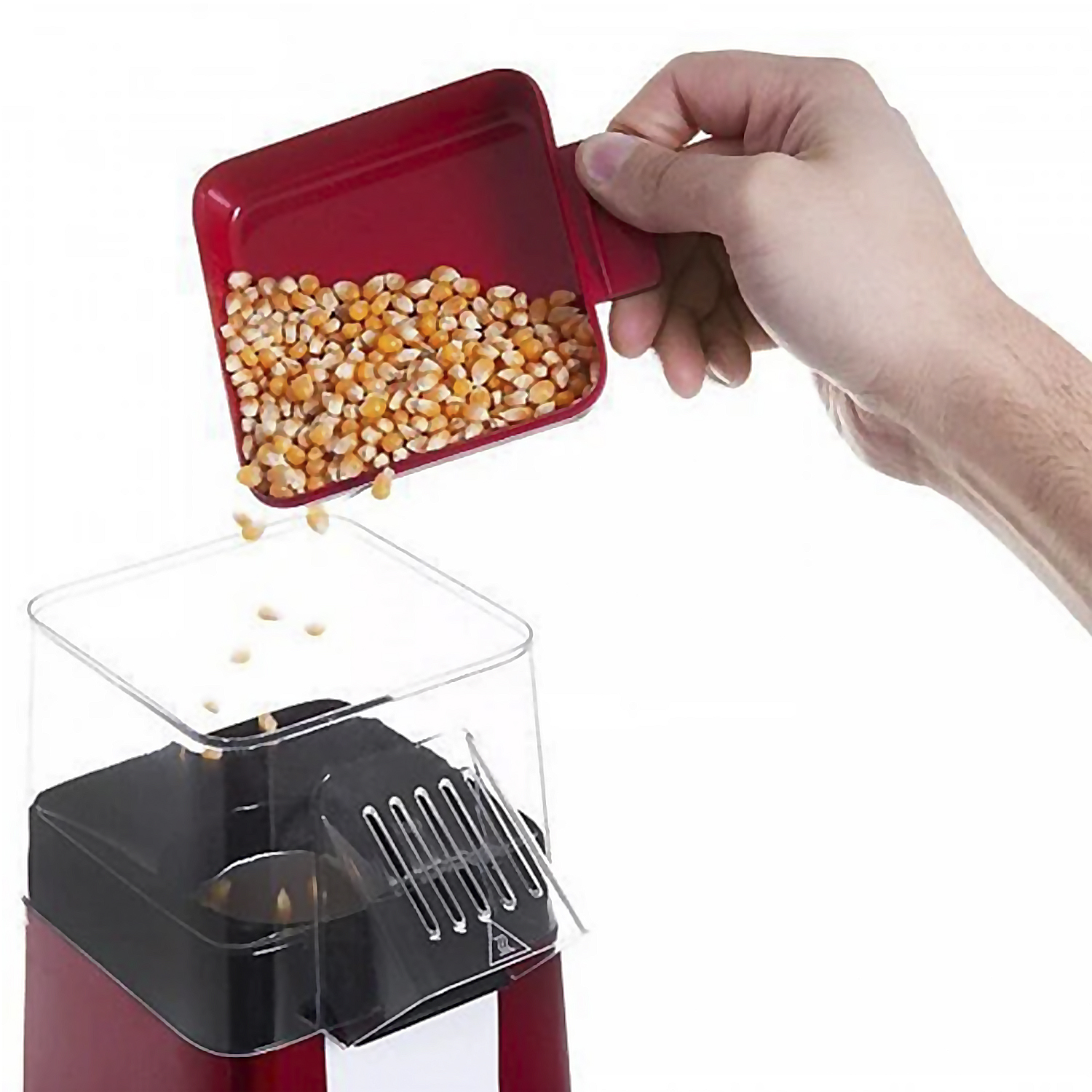 Una mano versa chicchi di mais da una paletta rossa in una macchina per popcorn. La macchina è rossa e nera, con un coperchio trasparente.