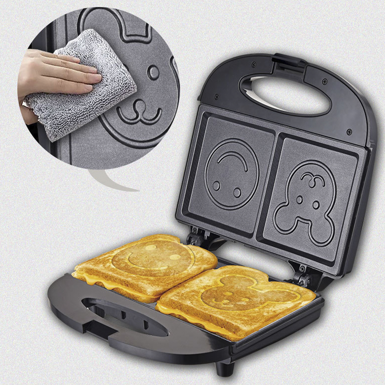 Una macchina per sandwich con pane a forma di faccina sorridente e orsetto. Una mano pulisce la parte superiore. Il pane ha formaggio fuso.
