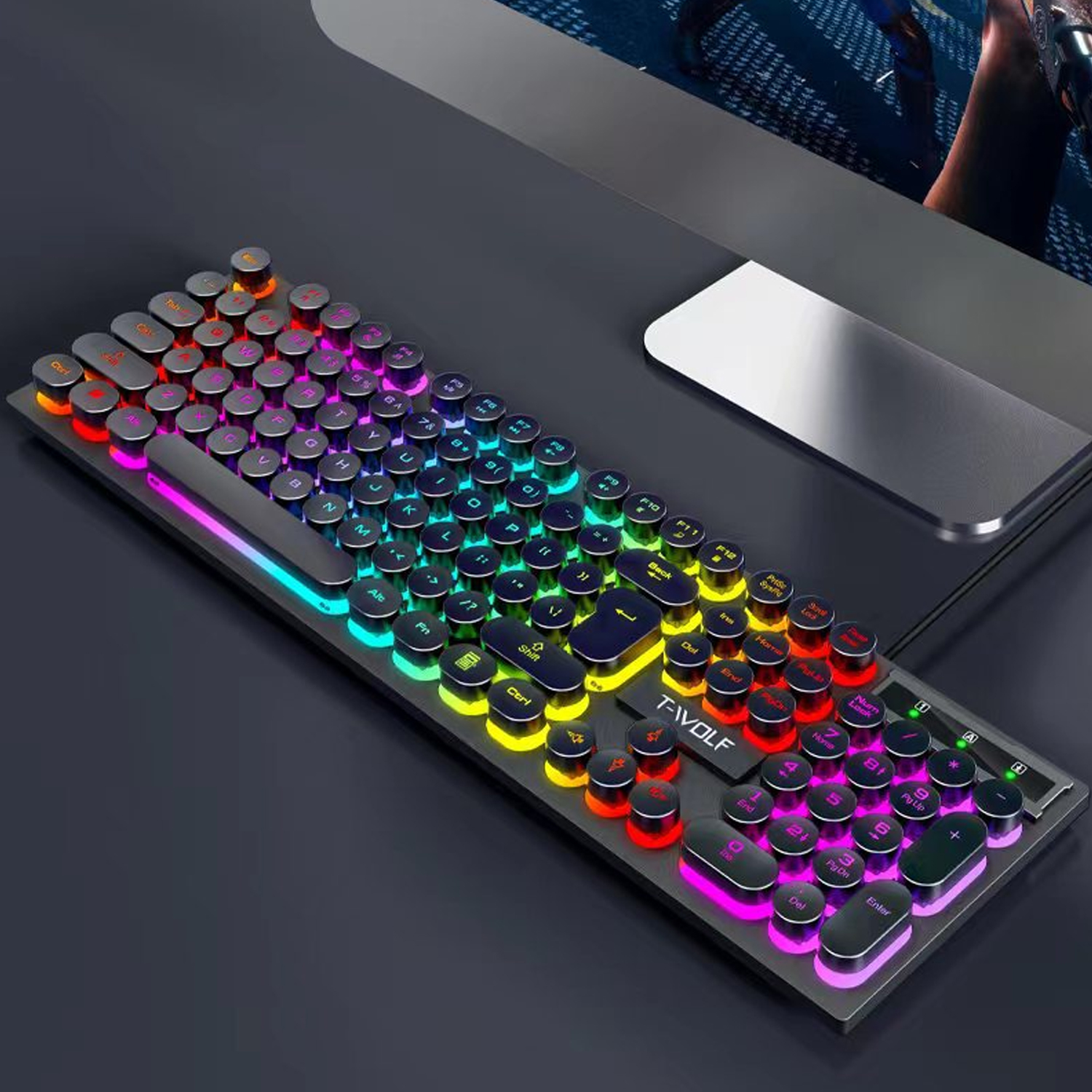 Eine Tastatur im Retro-Stil mit runden, beleuchteten Tasten in verschiedenen Farben. Sie liegt auf einer dunklen Oberfläche neben einem Monitor.