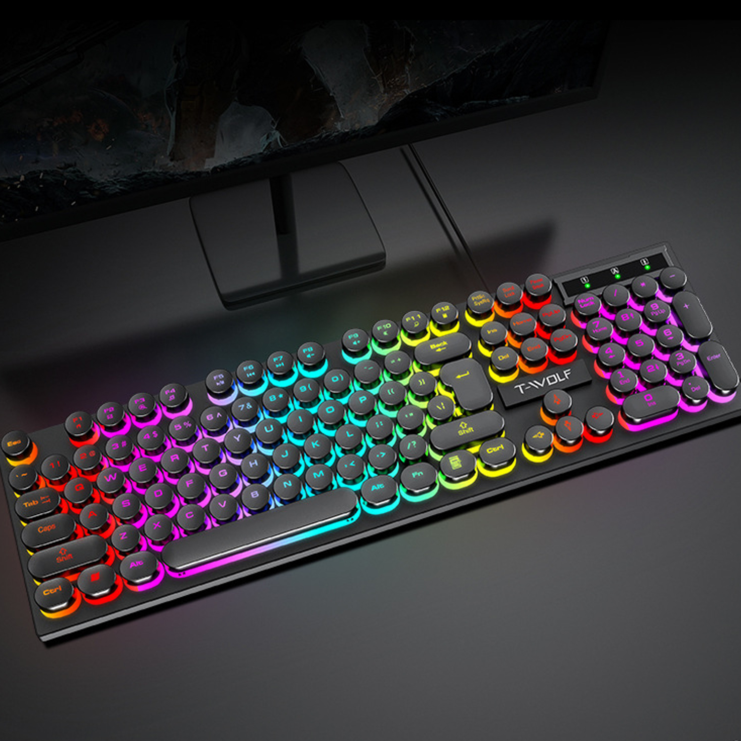 Eine schwarze Tastatur mit Regenbogenfarbenen Tasten liegt auf einer schwarzen Oberfläche. Ein Computermonitor ist im Hintergrund.