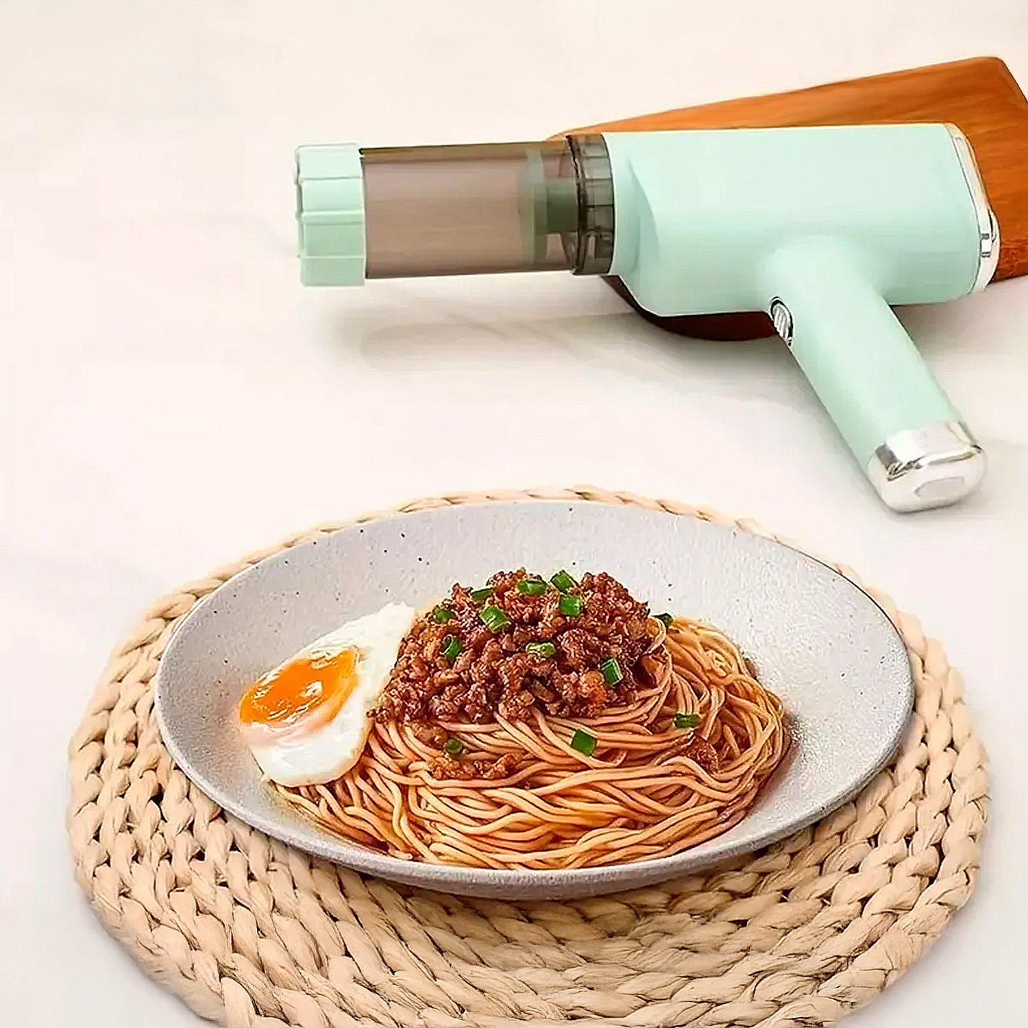Spaghetti con uovo e carne in un piatto, accanto a una macchina per la pasta. Gli spaghetti sono su un tappetino tessuto.